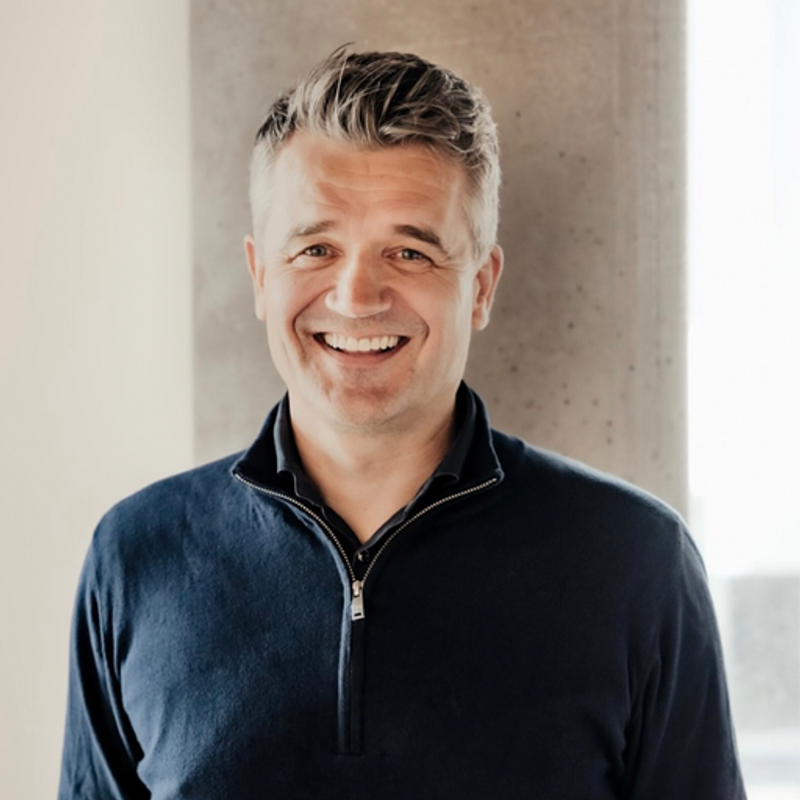 Headshot of a smiling man with grey hair in a dark blue quarter-zip shirt.