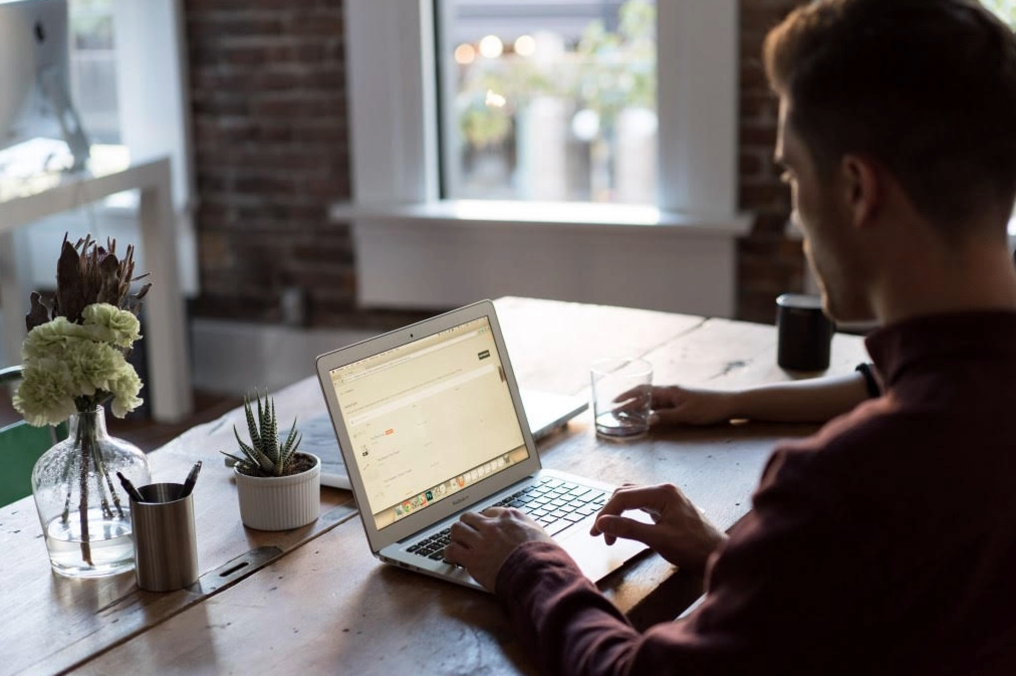 Person working on a laptop at a wooden desk with plants.