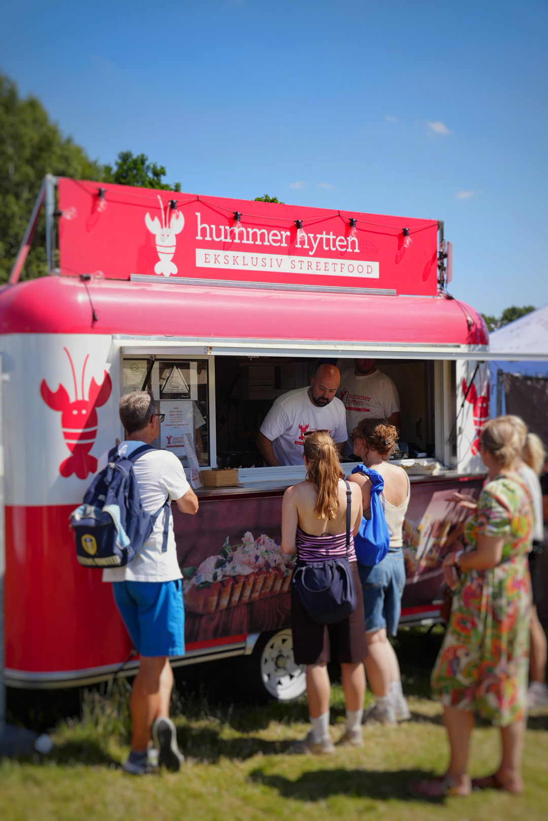 A red lobster-themed food truck with people ordering from a vendor on a sunny day.