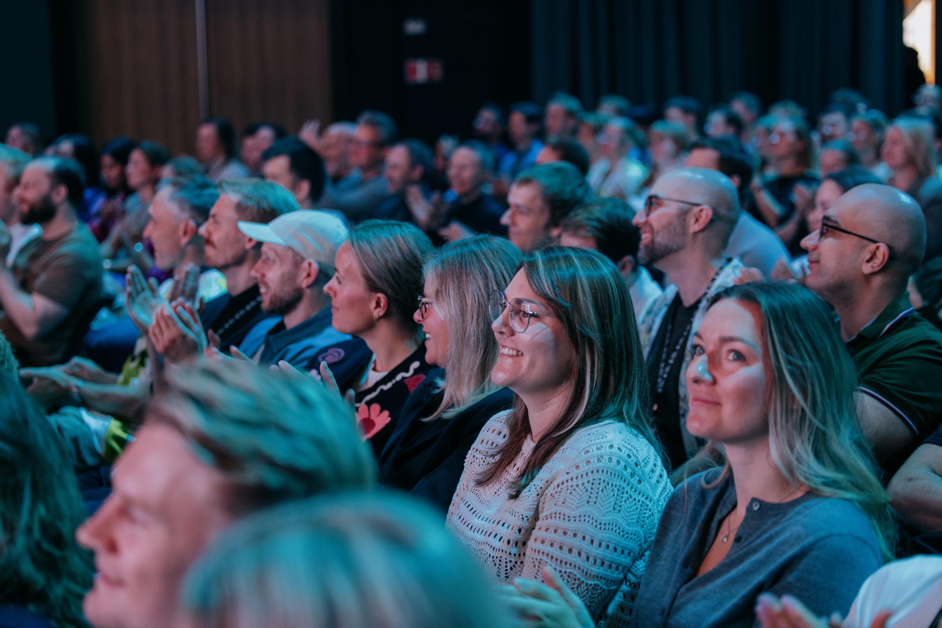An audience of people smiling and clapping during an event.