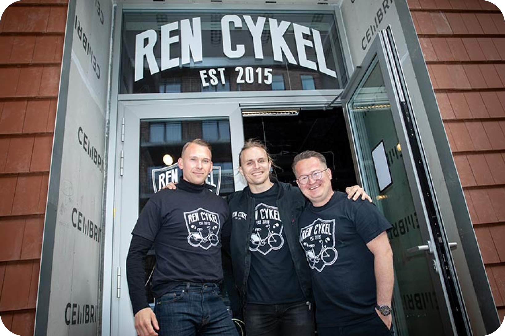 Three men smiling outside their 'REN CYKEL EST 2015' store.