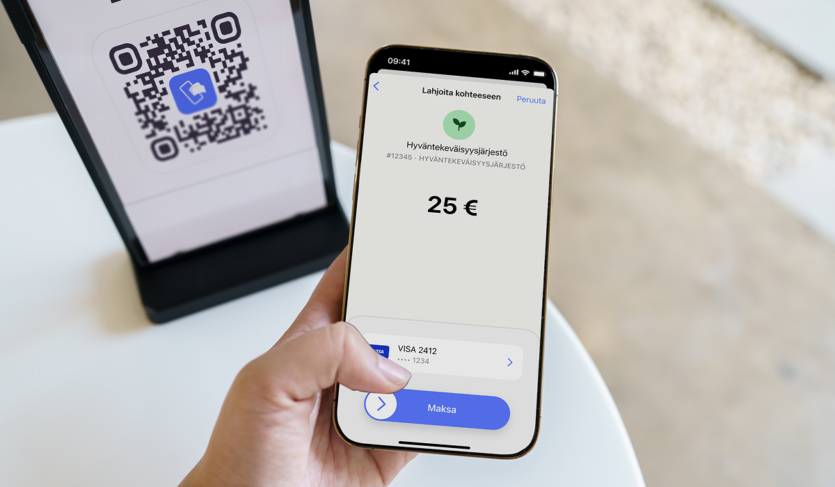 A hand holds a smartphone displaying a 25 euro donation payment to a charity, with a QR code sign in the background.