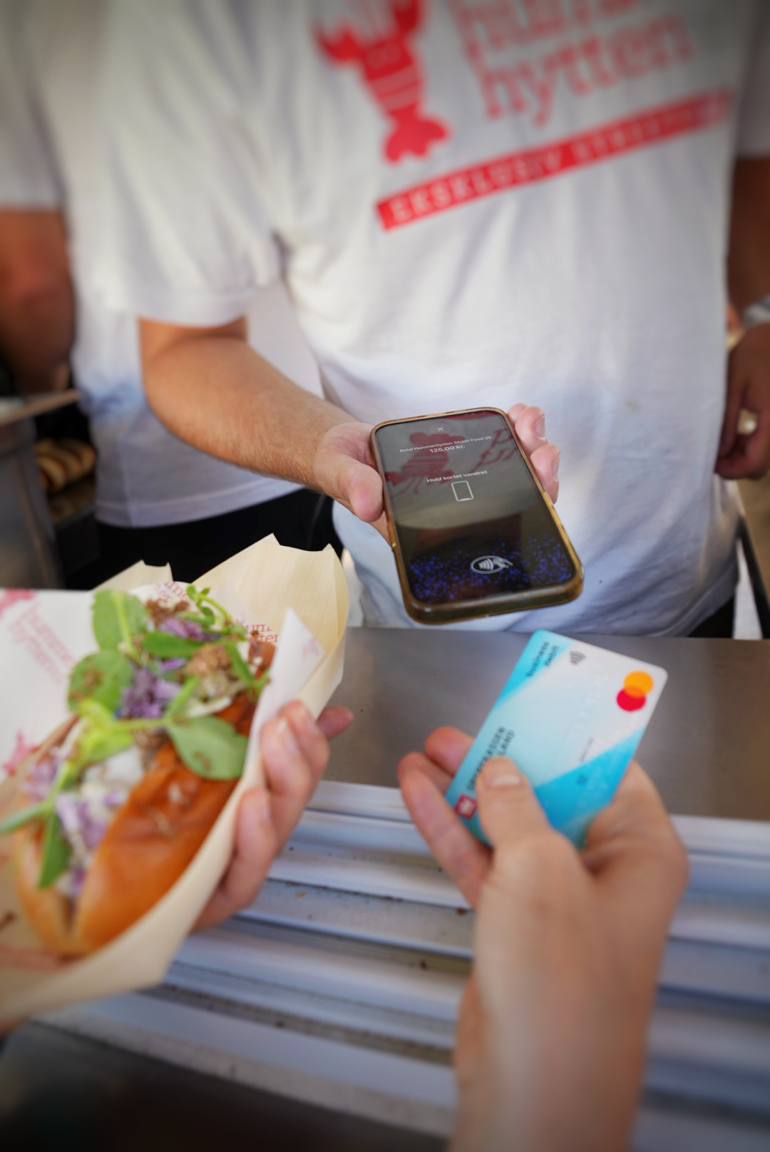 A customer taps a credit card on a vendor's smartphone to pay for a food roll.