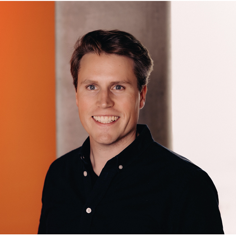 Smiling young man in a black shirt against an orange and light wall background.