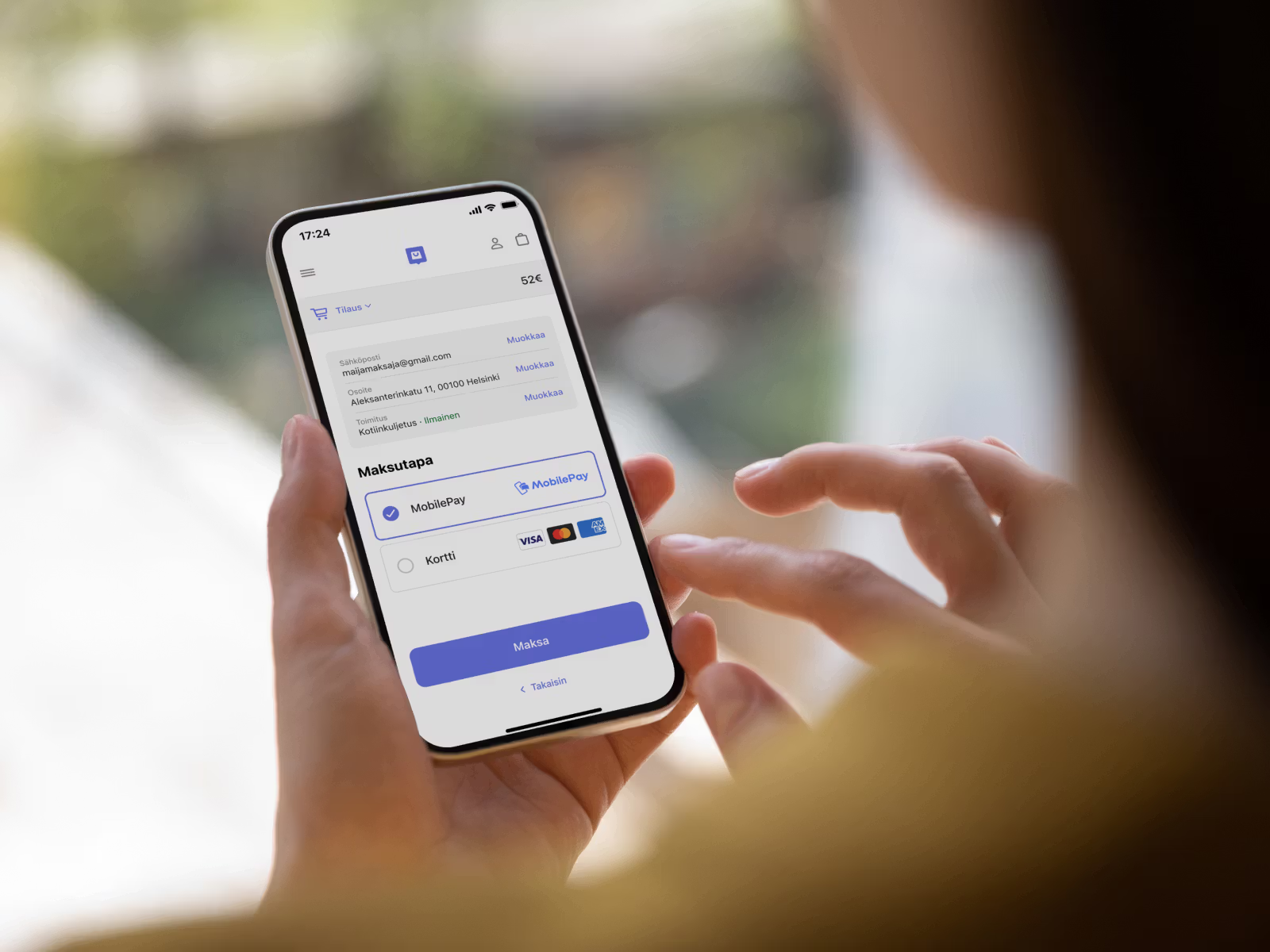 Hands hold a smartphone displaying a MobilePay payment screen in Finnish.