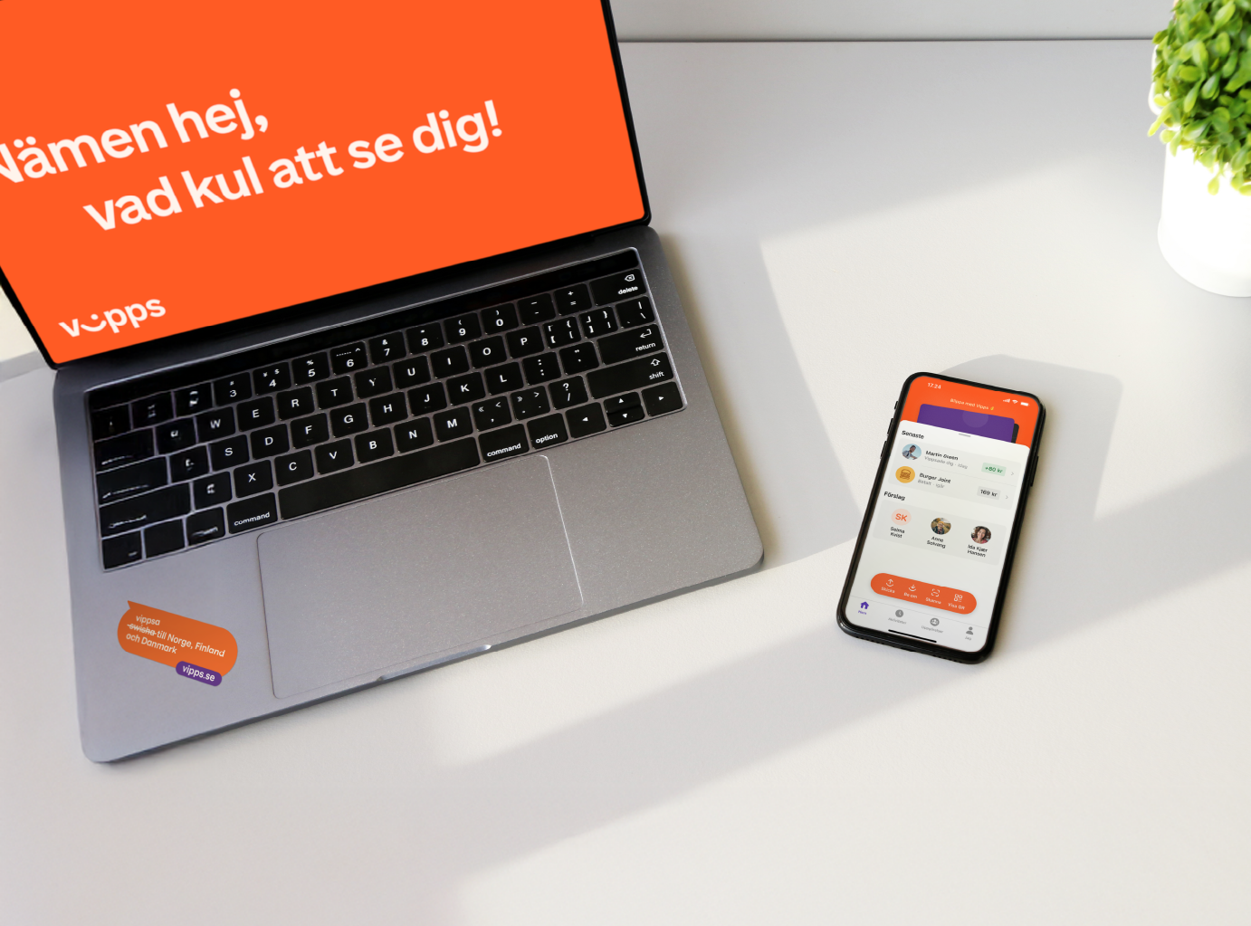 A laptop and smartphone displaying the Vipps app on a white desk with potted plants.