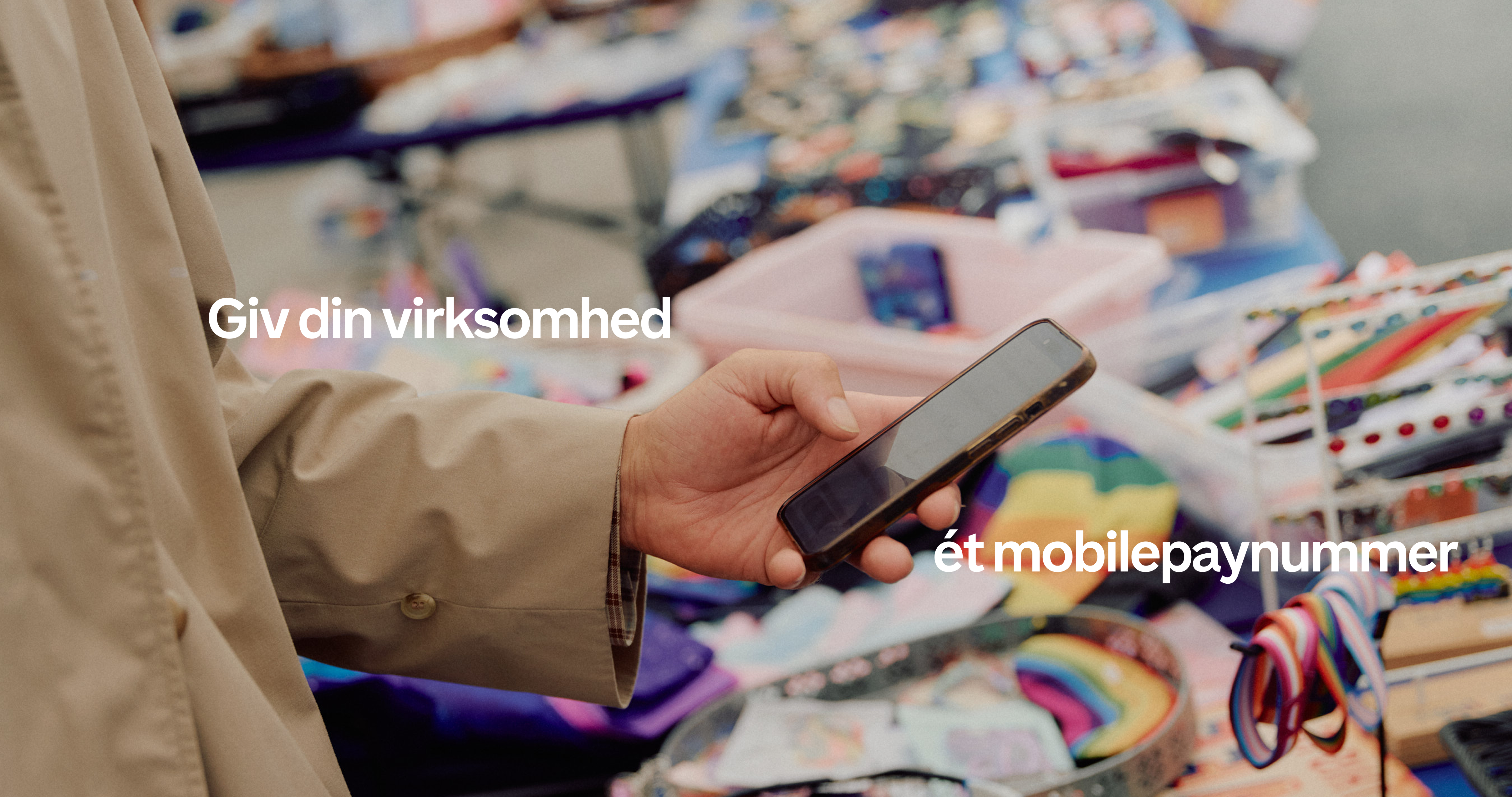 Person holding a smartphone at a market stall with text "Giv din virksomhed ét mobilepaynummer".