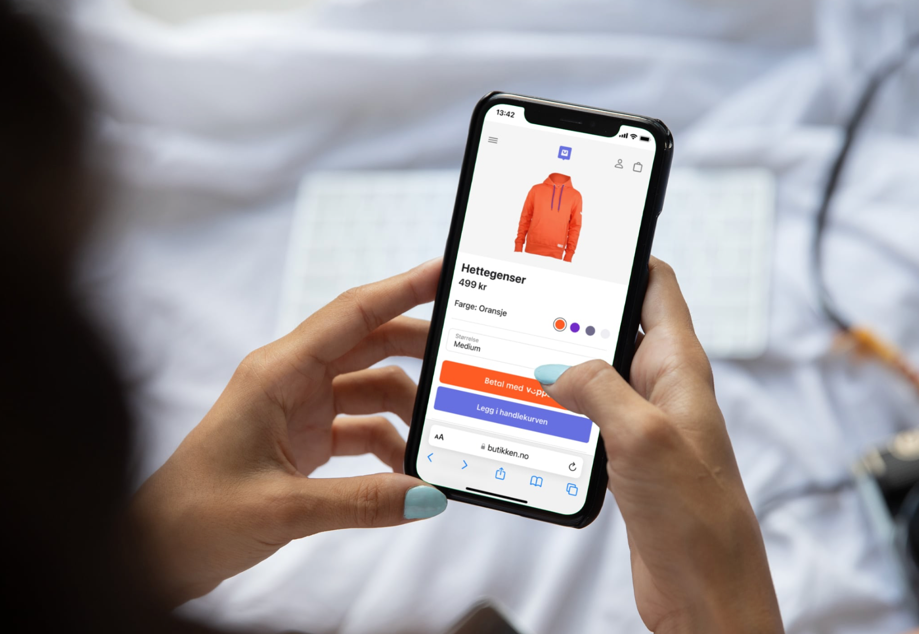 Hands holding a smartphone displaying an e-commerce product page for an orange hoodie.