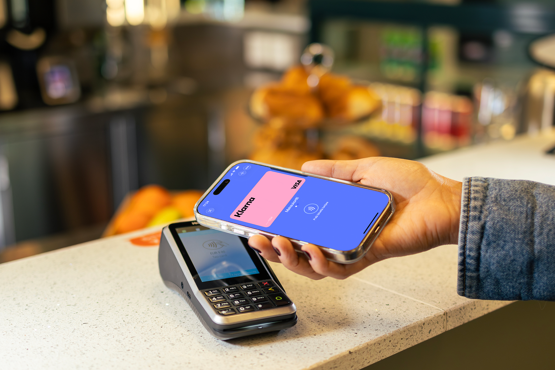 A person uses a smartphone with the MobilePay app open to make a contactless payment at a terminal.