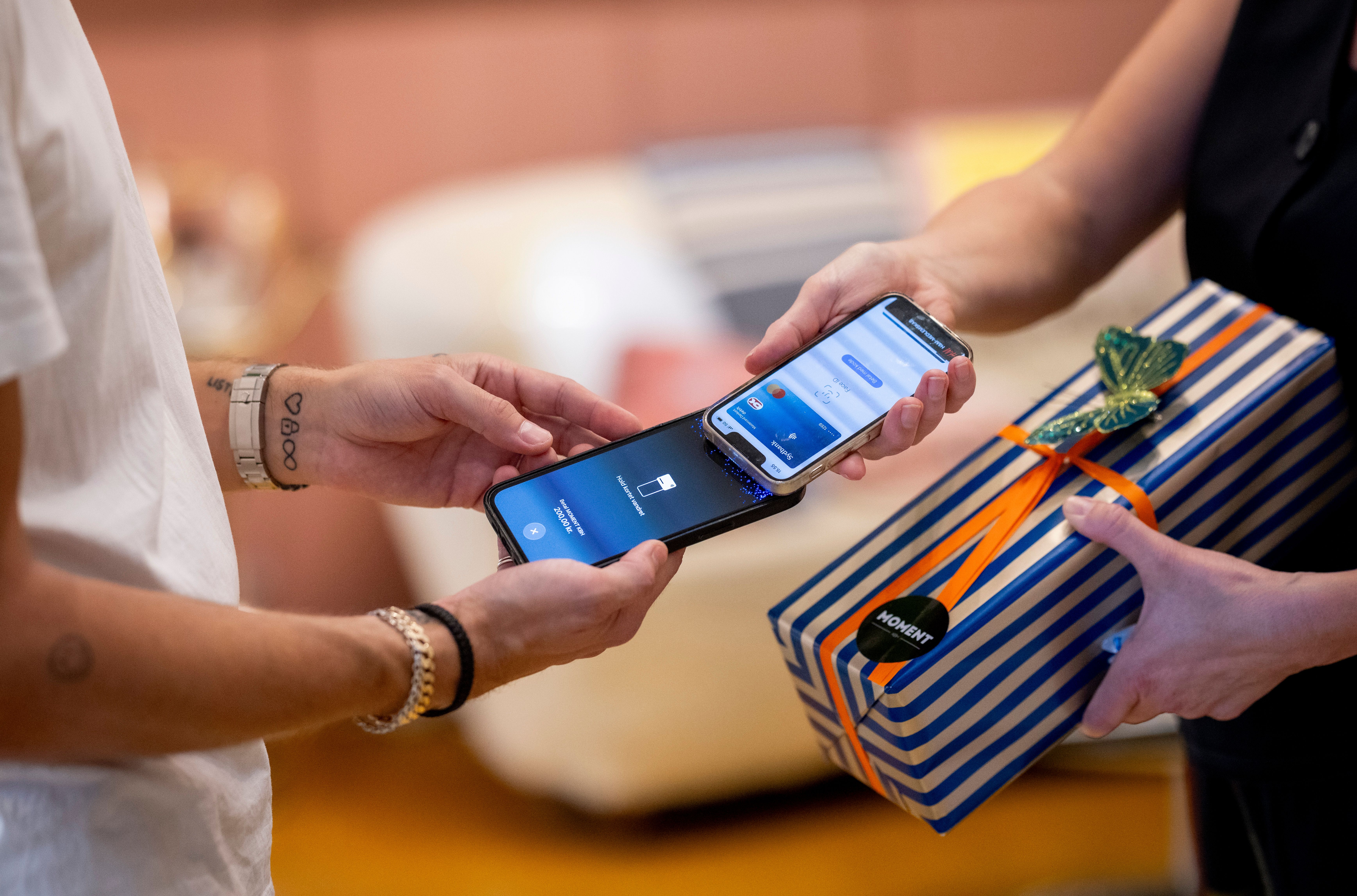 Two smartphones interact for a contactless payment, next to a striped gift box.