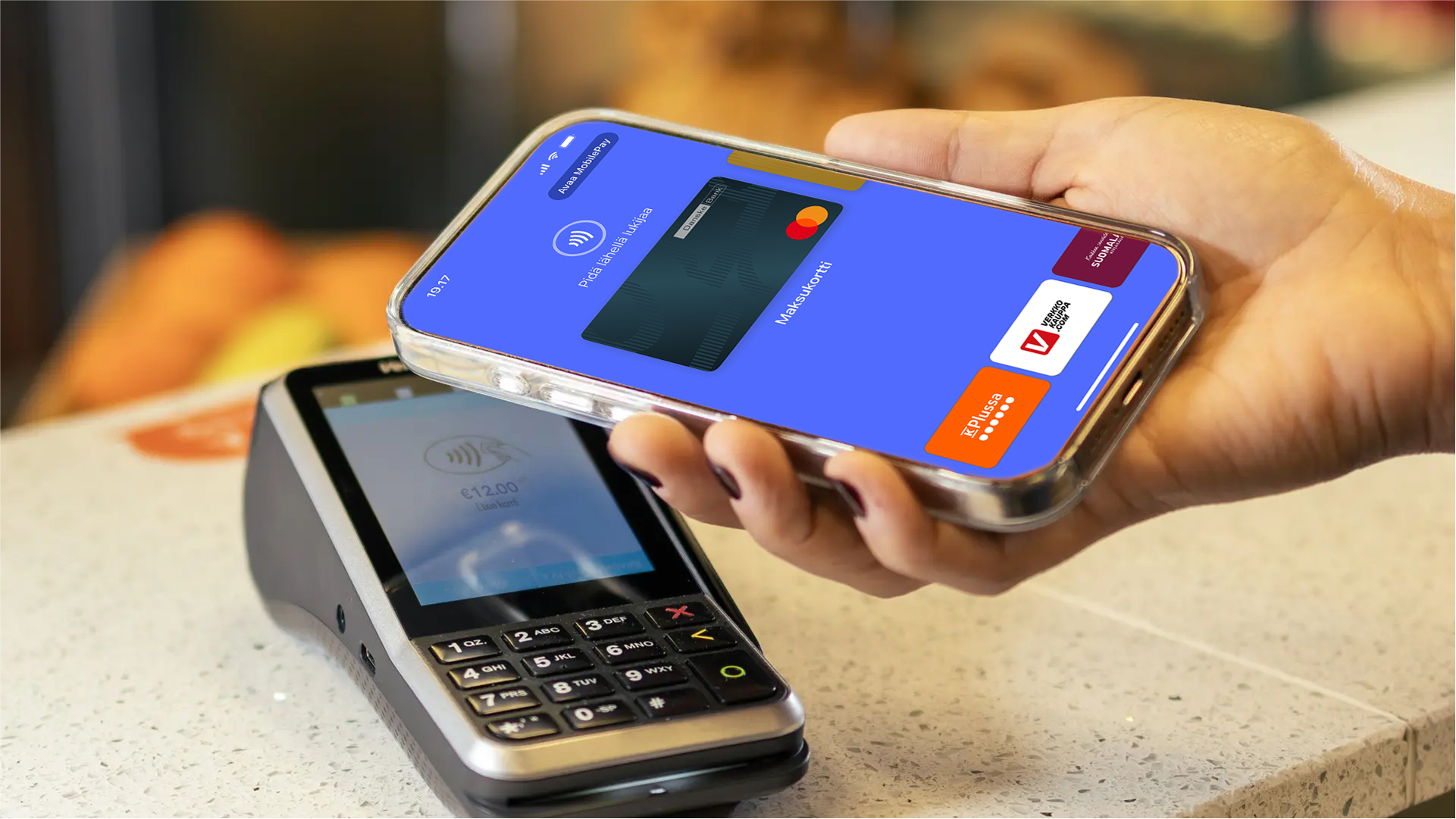 A hand holding a smartphone with a digital wallet open, making a contactless payment at a terminal displaying €13.00.