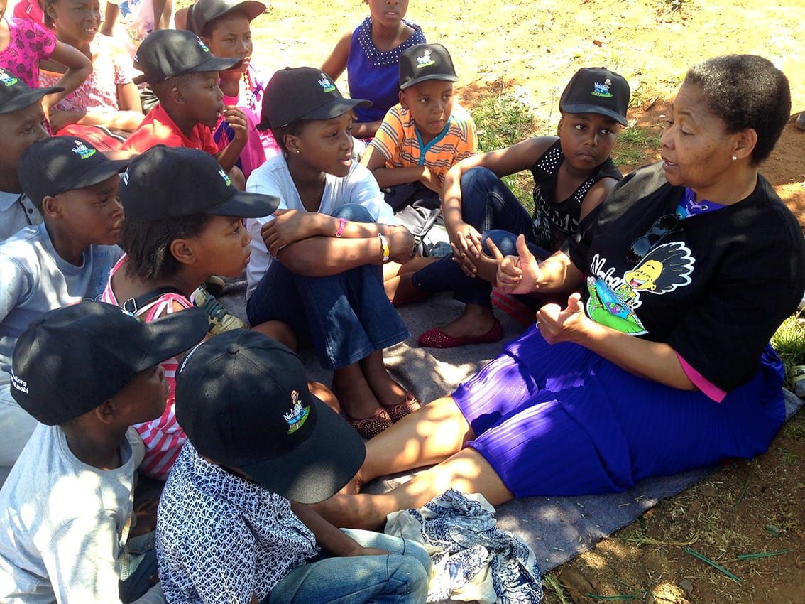 A teacher giving a class sat outside on the grass to a group of students