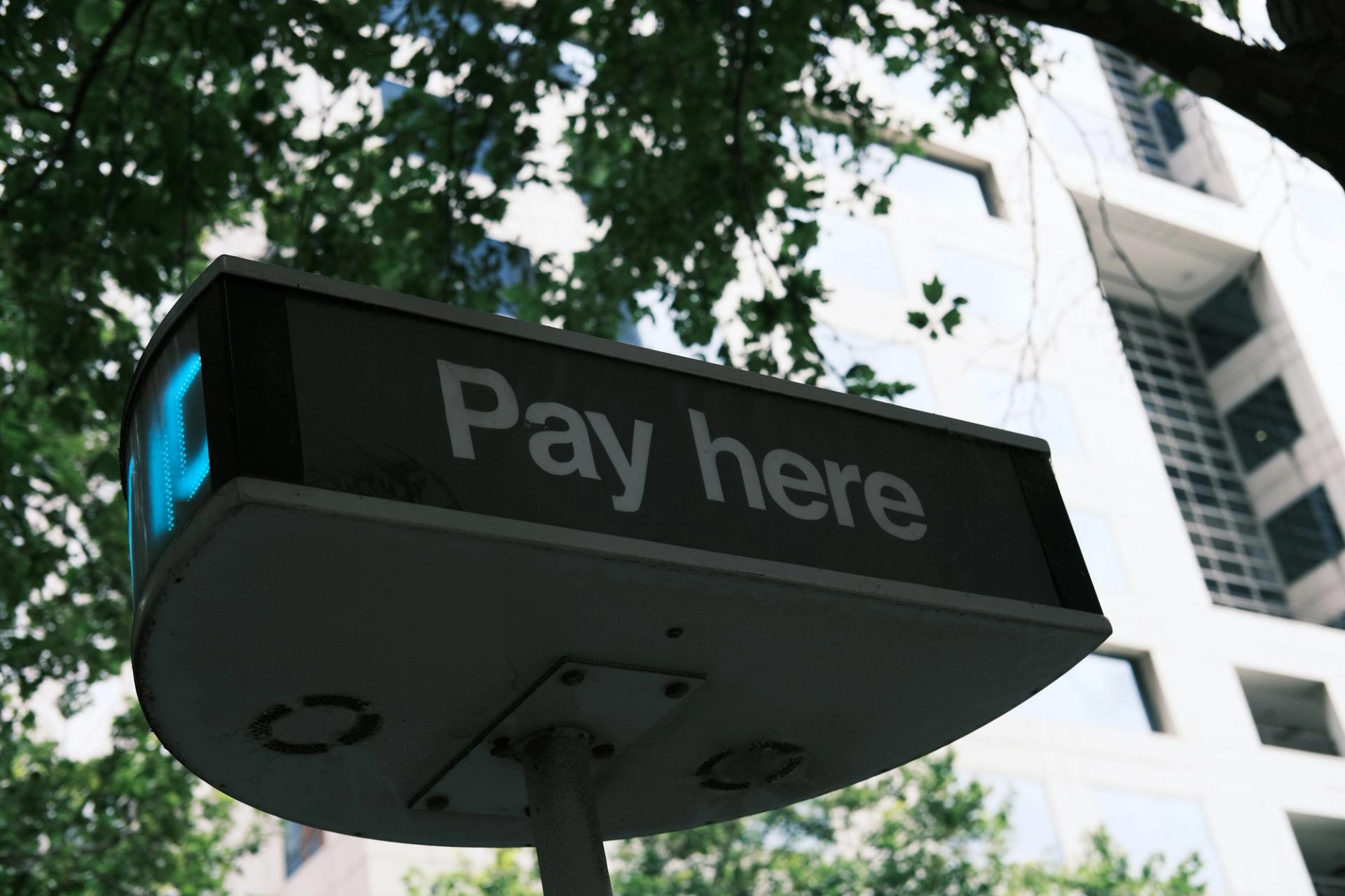 a pay here sign is sitting under a tree in front of a building .