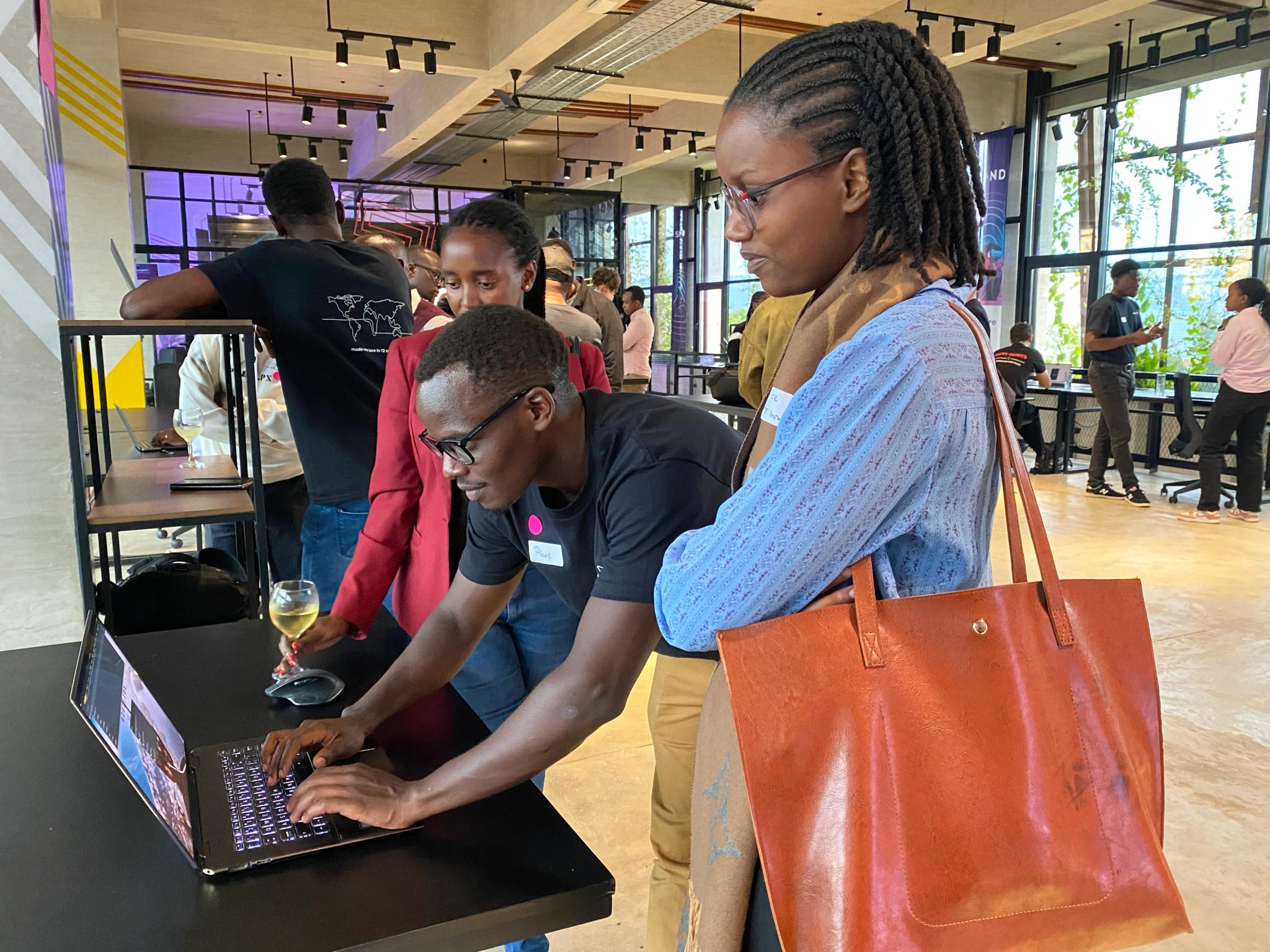 a group of people are standing around a table looking at a laptop computer .