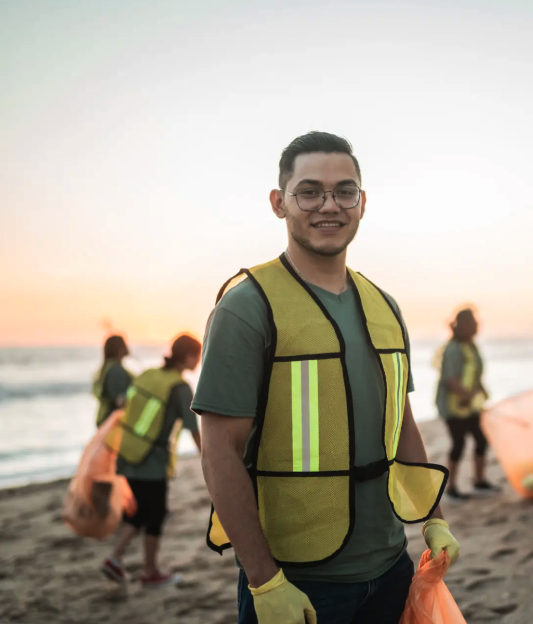 An image of a man in a fluorescent jacket on the beach doing clean up
