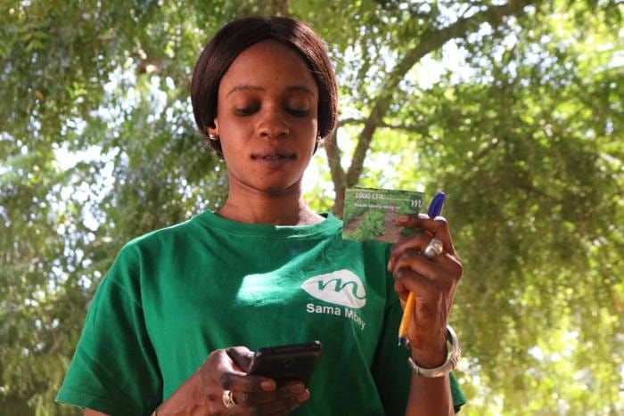 A woman looking at her phone with a card in her hand.