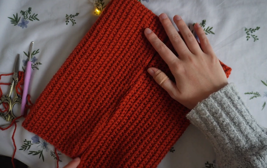 Crocheted orange piece of fabric, folded so the edges meet in the centre