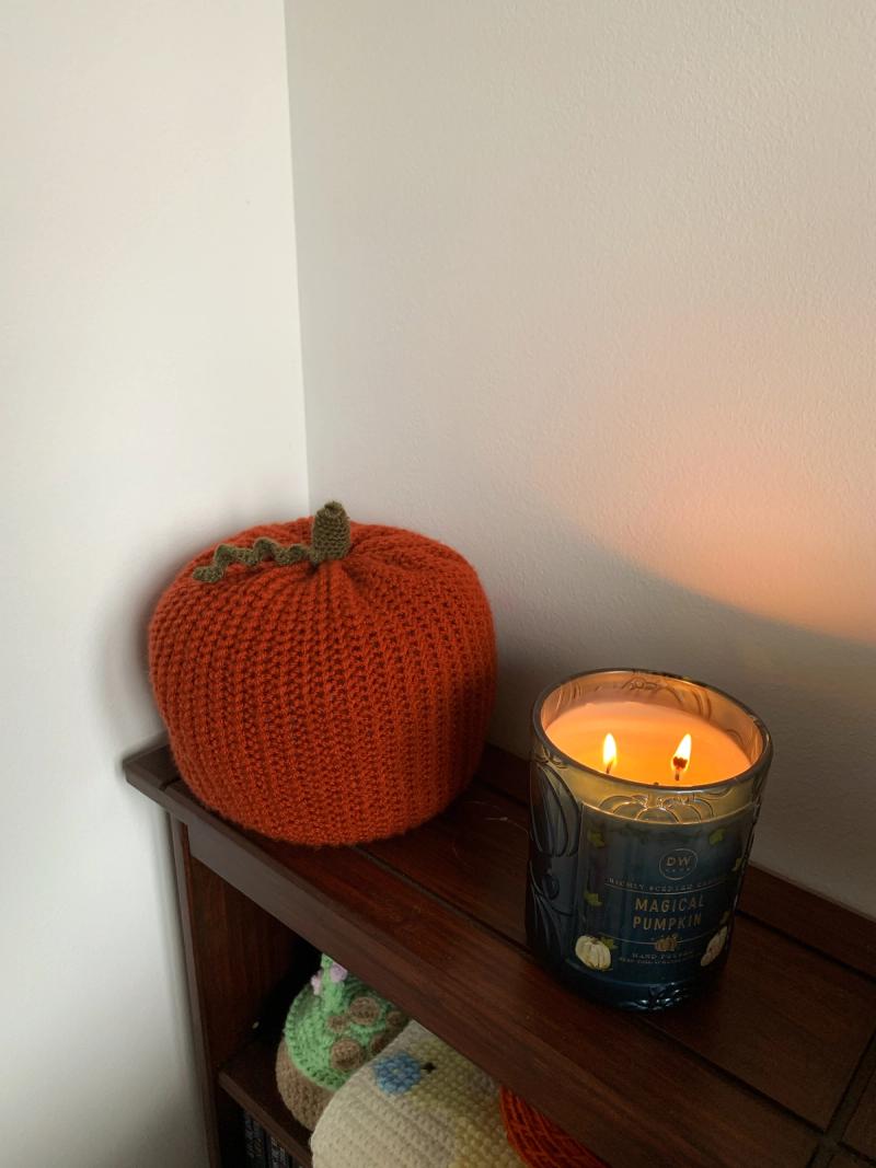 Large crocheted pumpkin sat on a bookshelf, with a Halloween candle sat beside it to set the ambience.