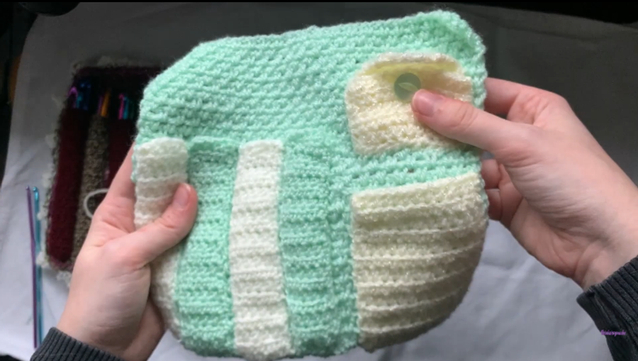 Large flat square panel of the moss stitch, with 4 hook pockets sewn side by side to the left, the scissor pocket sewn to the right, the button pocket with flap sewn down first, with the front of the button pocket sewn on top of this (with a button).