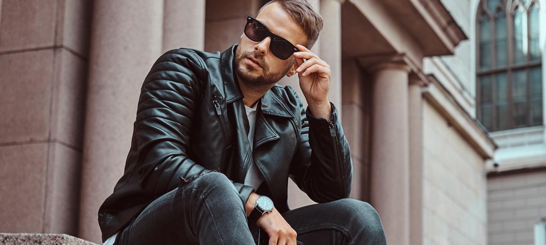 A man in a leather jacket and sunglasses witting on stone steps in front of stone columns