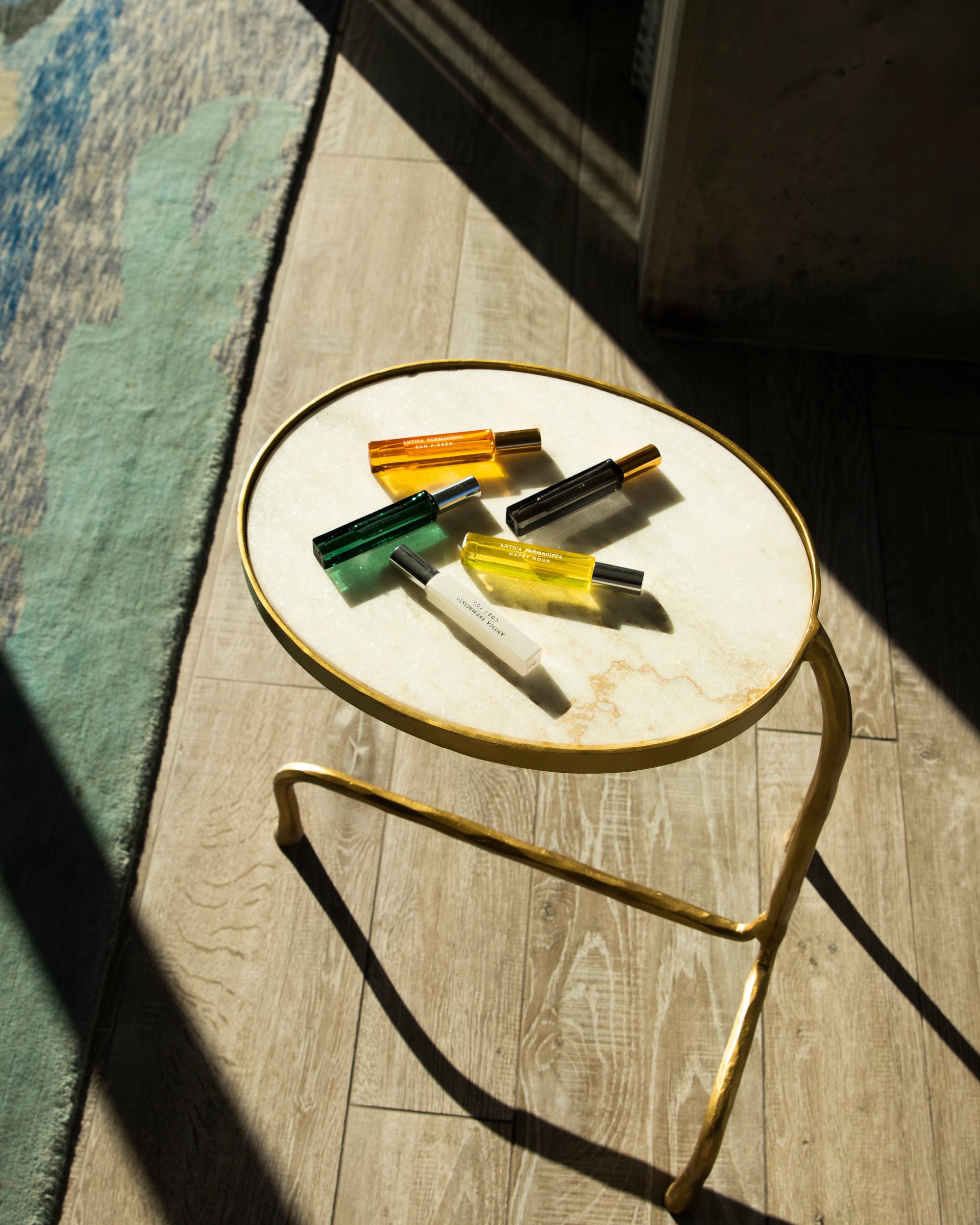 Antica Farmacista fine fragrance rollerballs arranged on a gold and marble side table in raking sunlight.