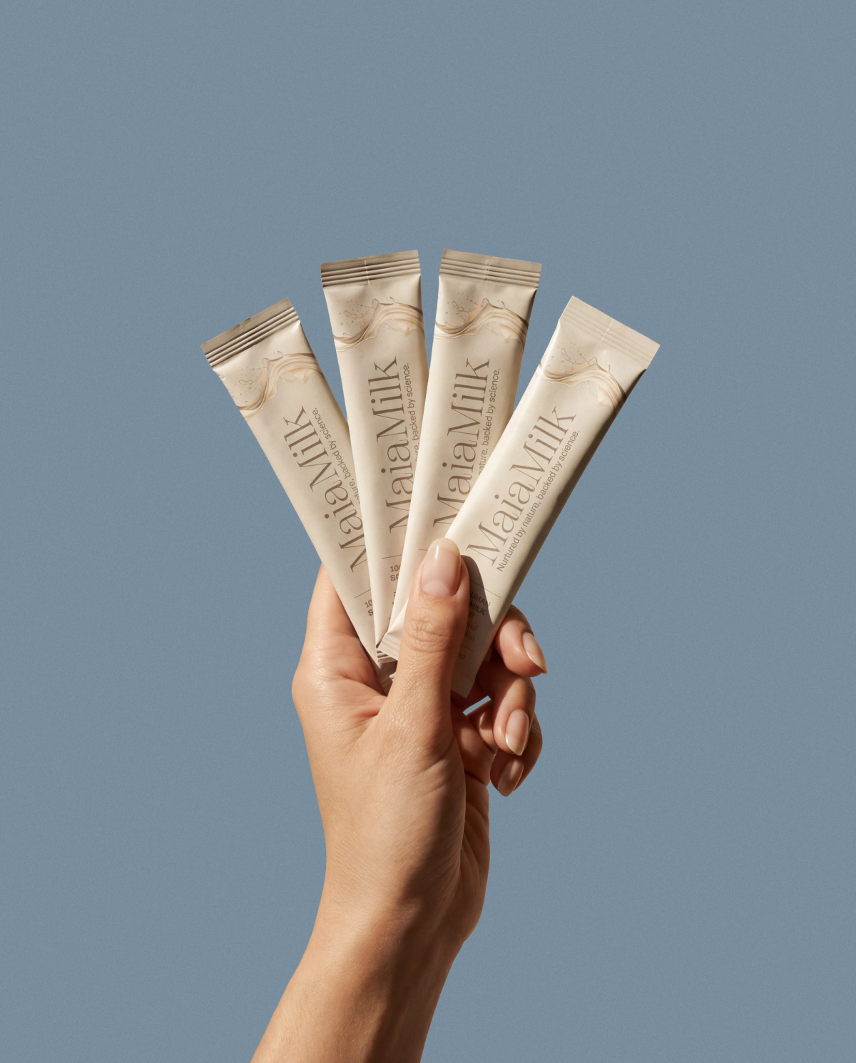 A hand holding several MaiaMilk packets against a cool blue field.