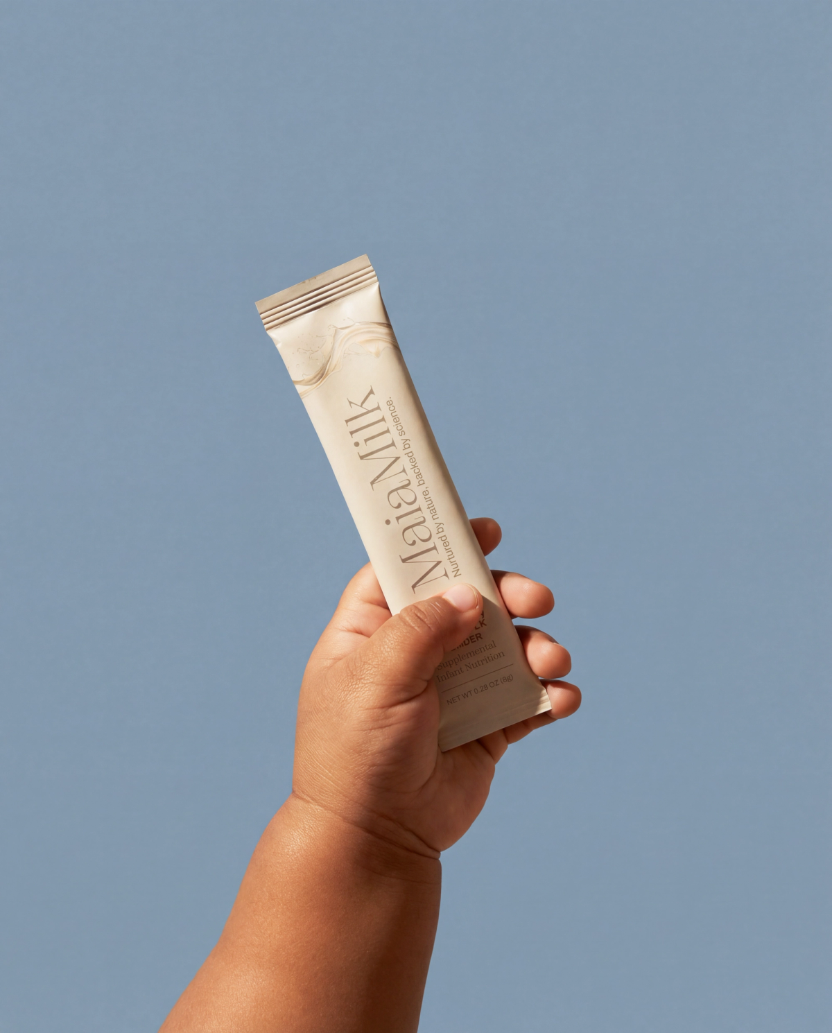 A hand holding a single MaiaMilk packet against a cool blue background.