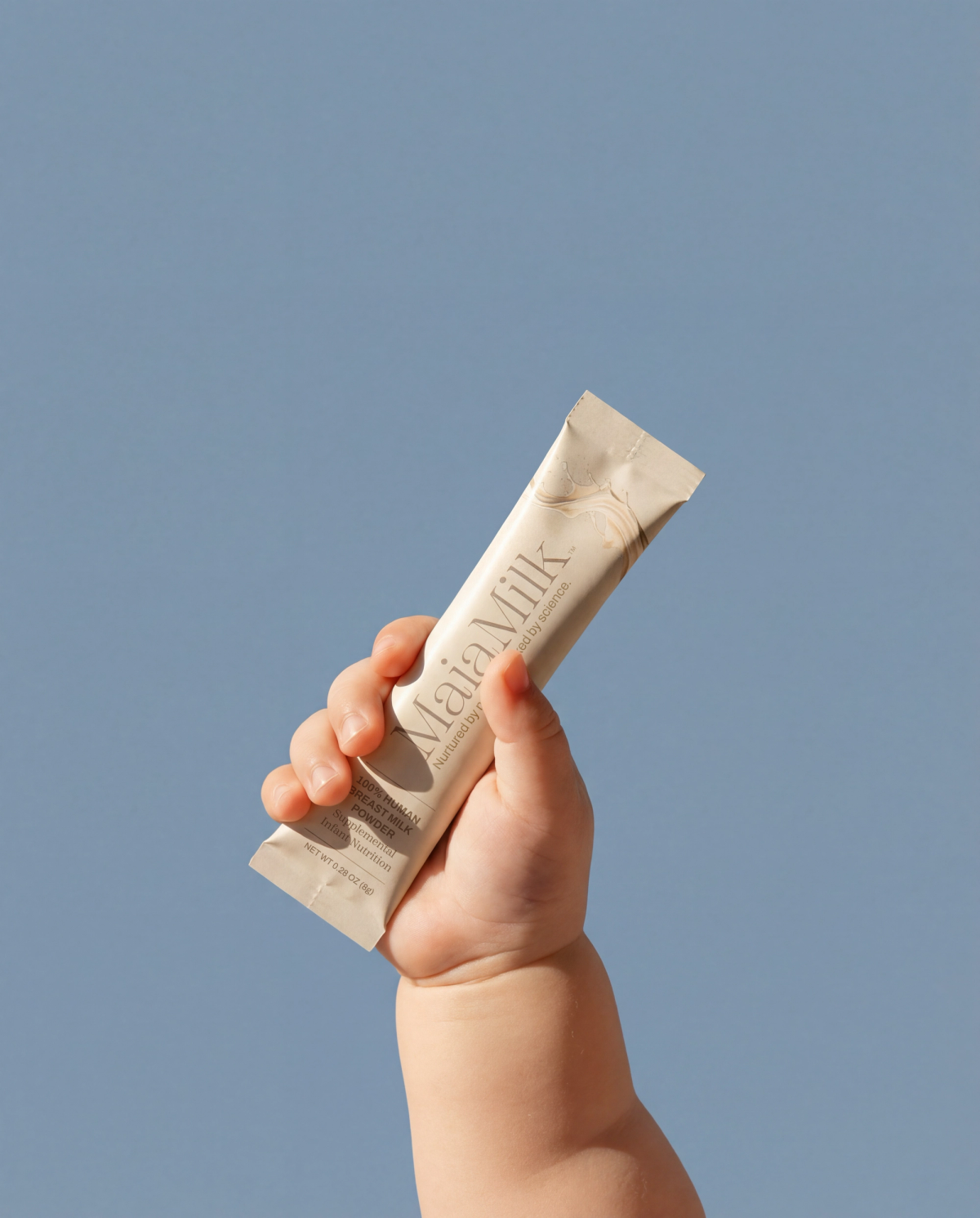 A small child’s hand holding a MaiaMilk packet against a cool blue field.
