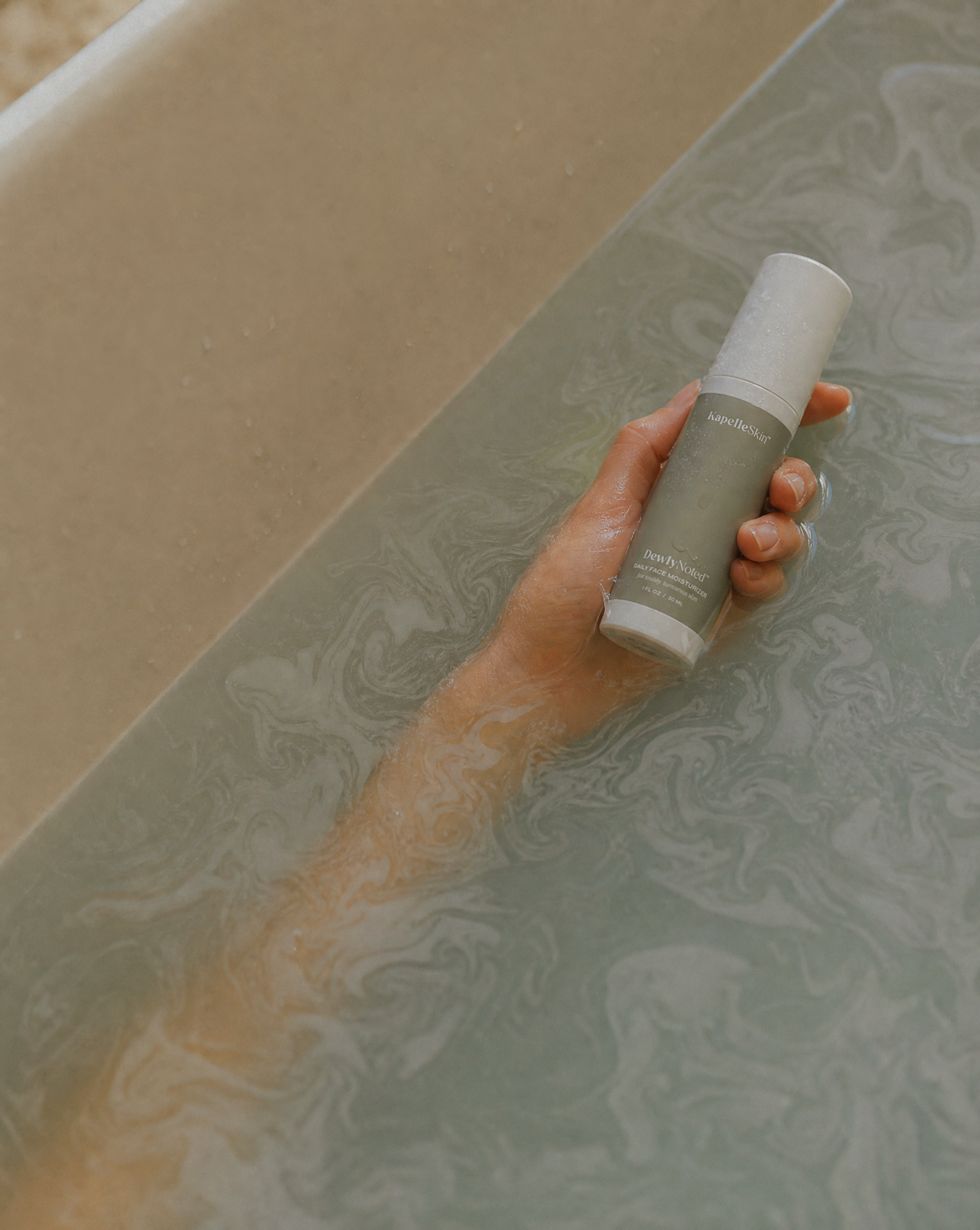 An arm moving through milky water while holding the KapelleSkin bottle.
