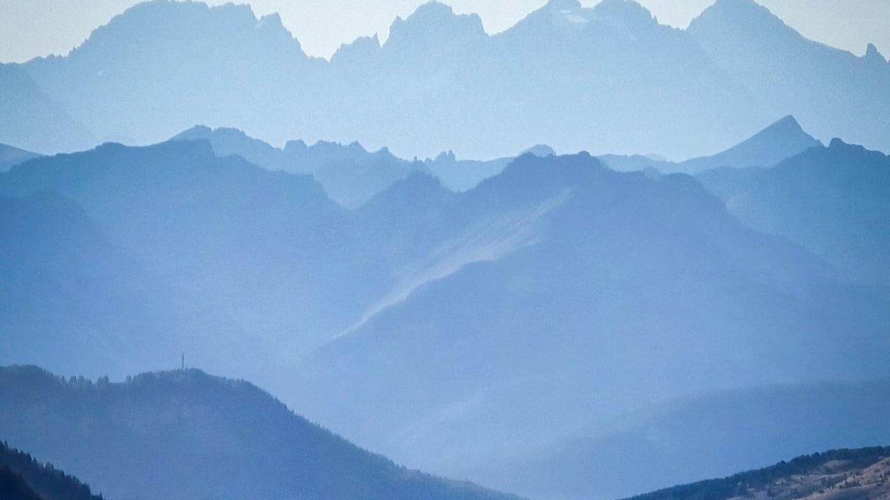 Layered blue mountain ranges fading into soft mist, with distant peaks rising beneath