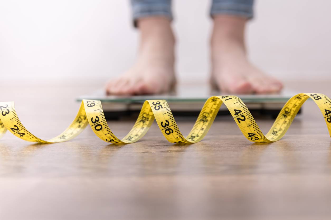 A pair of feet, standing on scales. A measuring tape is on the floor in front