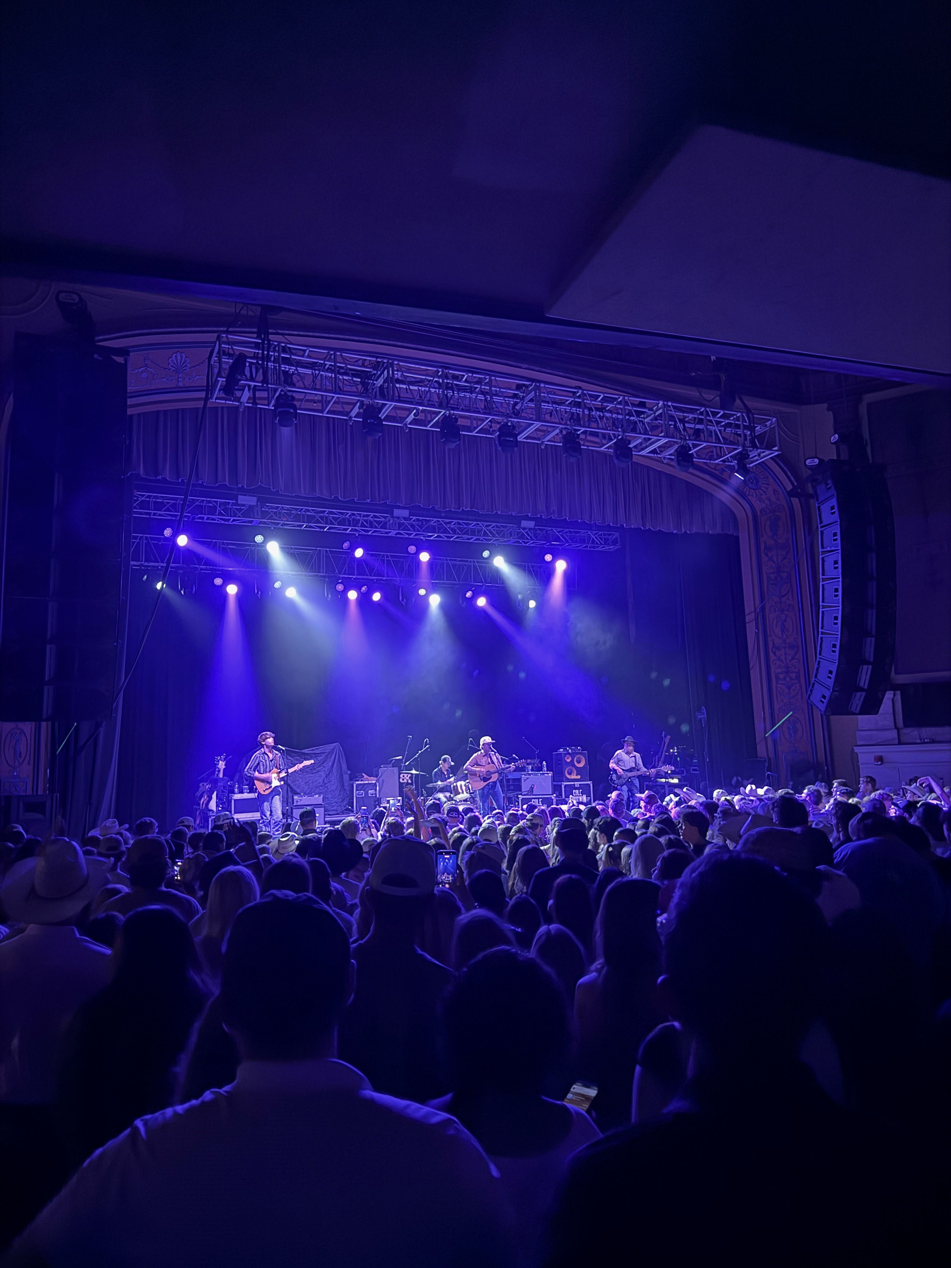 Live concert with the band on a blue-lit stage seen from within the crowd