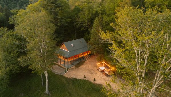 Forest cabin with an illuminated outdoor dining area at dusk