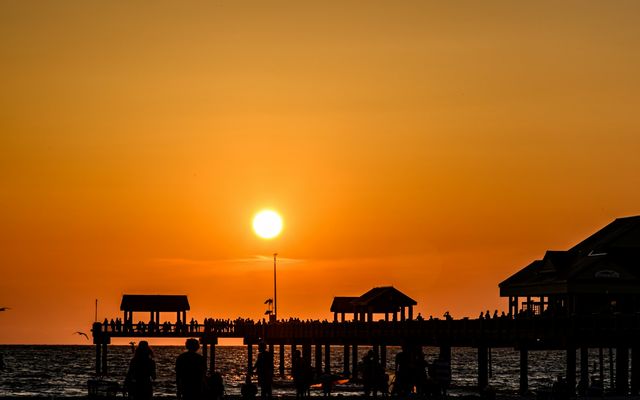 the sun is setting over a pier on the beach
