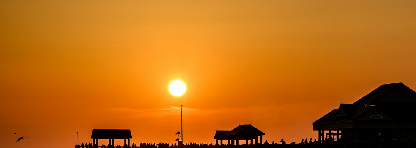 the sun is setting over a pier on the beach