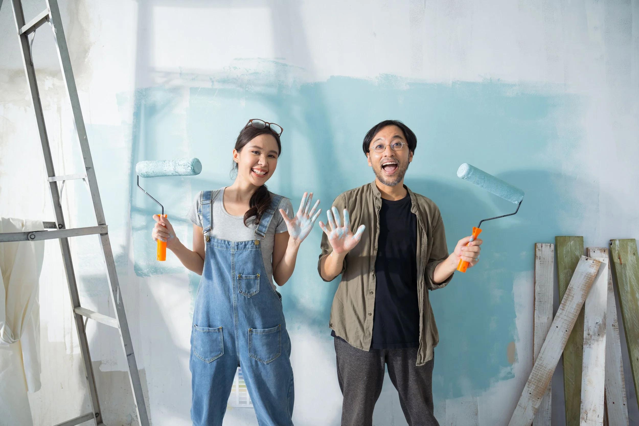 Asian couple with paint rollers repainting their home before selling it