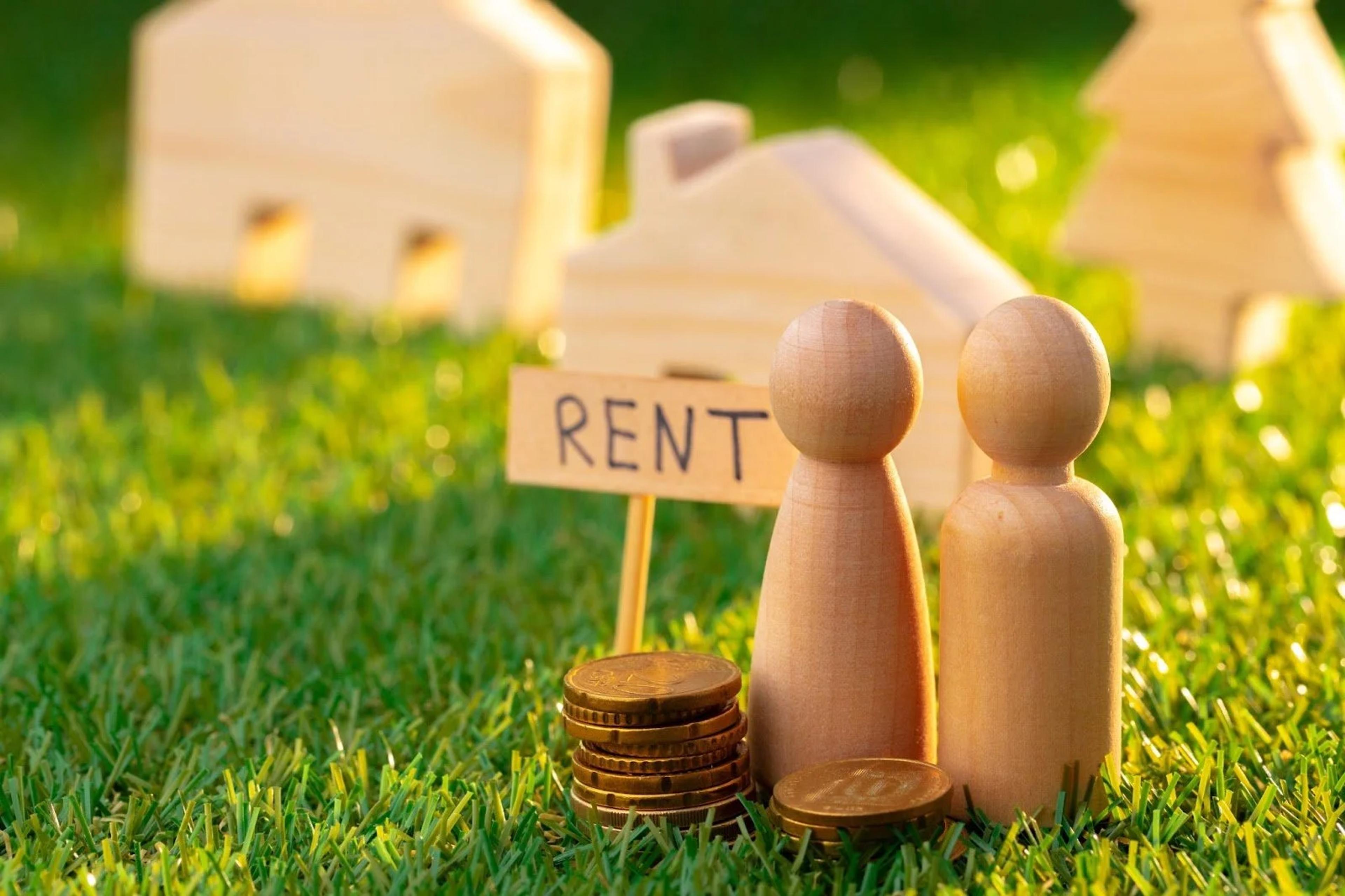 Wooden figures by a RENT sign and coins in front of model houses