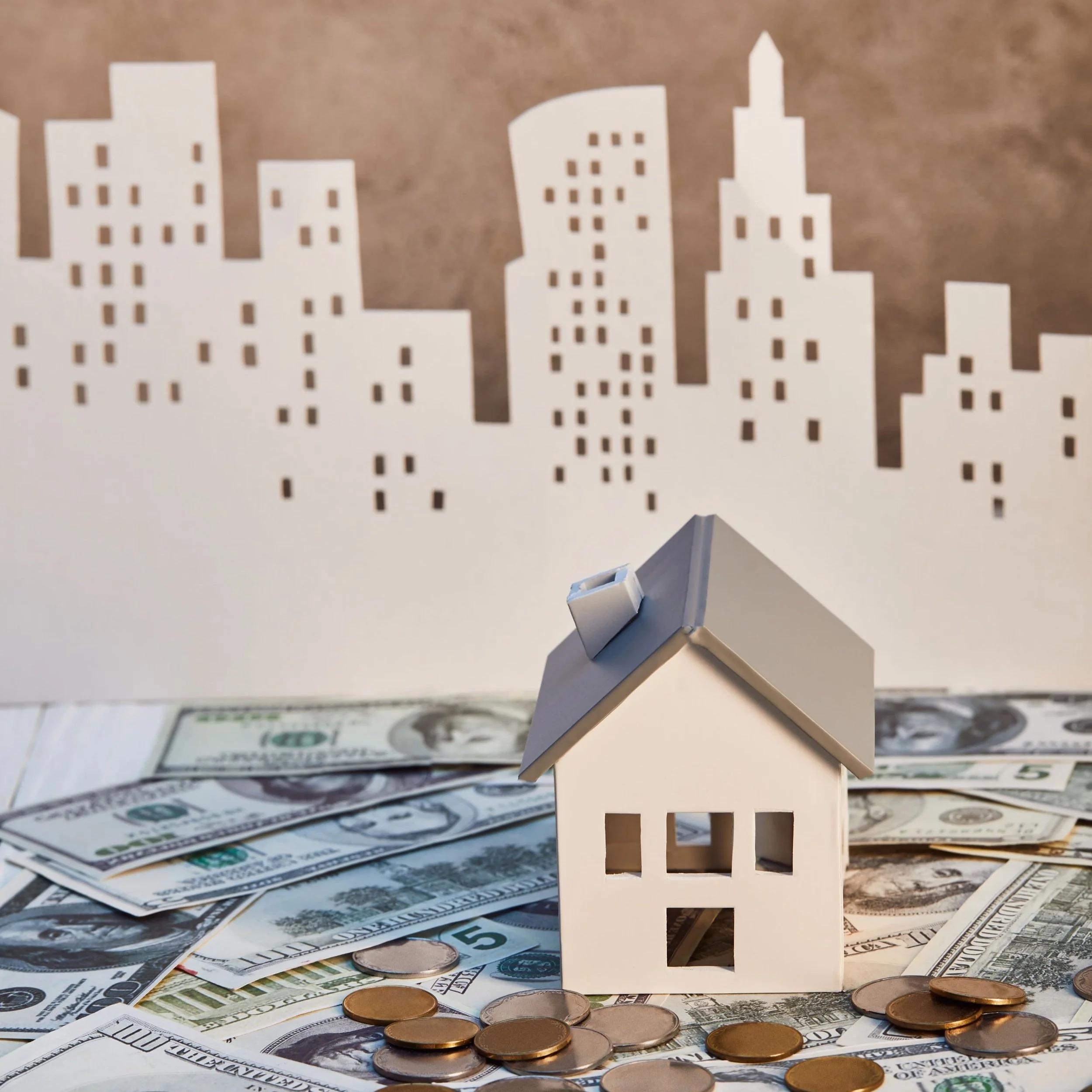 Model house on banknotes and coins in front of a paper city skyline: real estate investment for first-timers