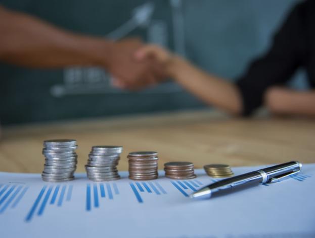 Handshake behind stacks of coins and financial charts after an investment deal