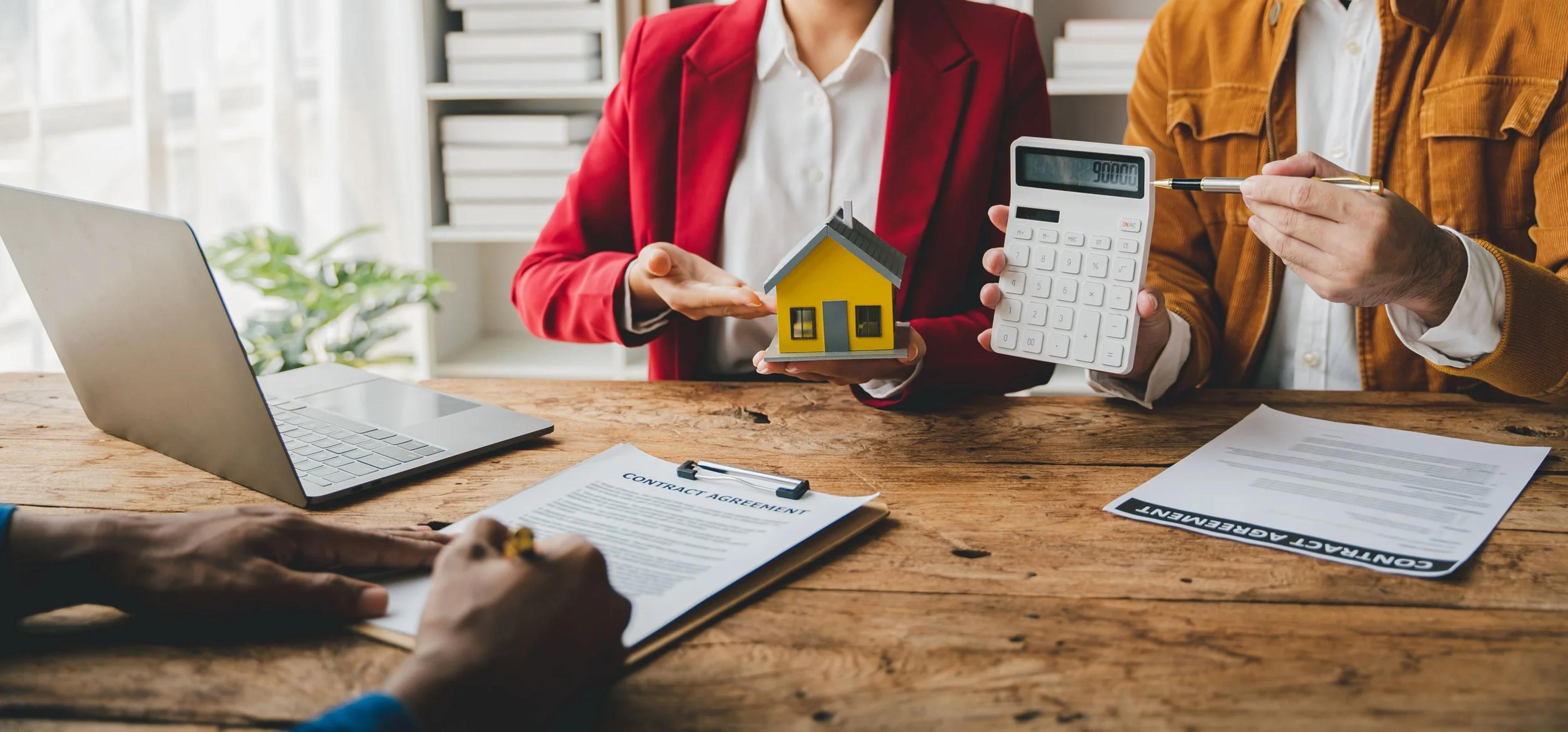 Property agent with a house model and calculator going through a sale contract with a client