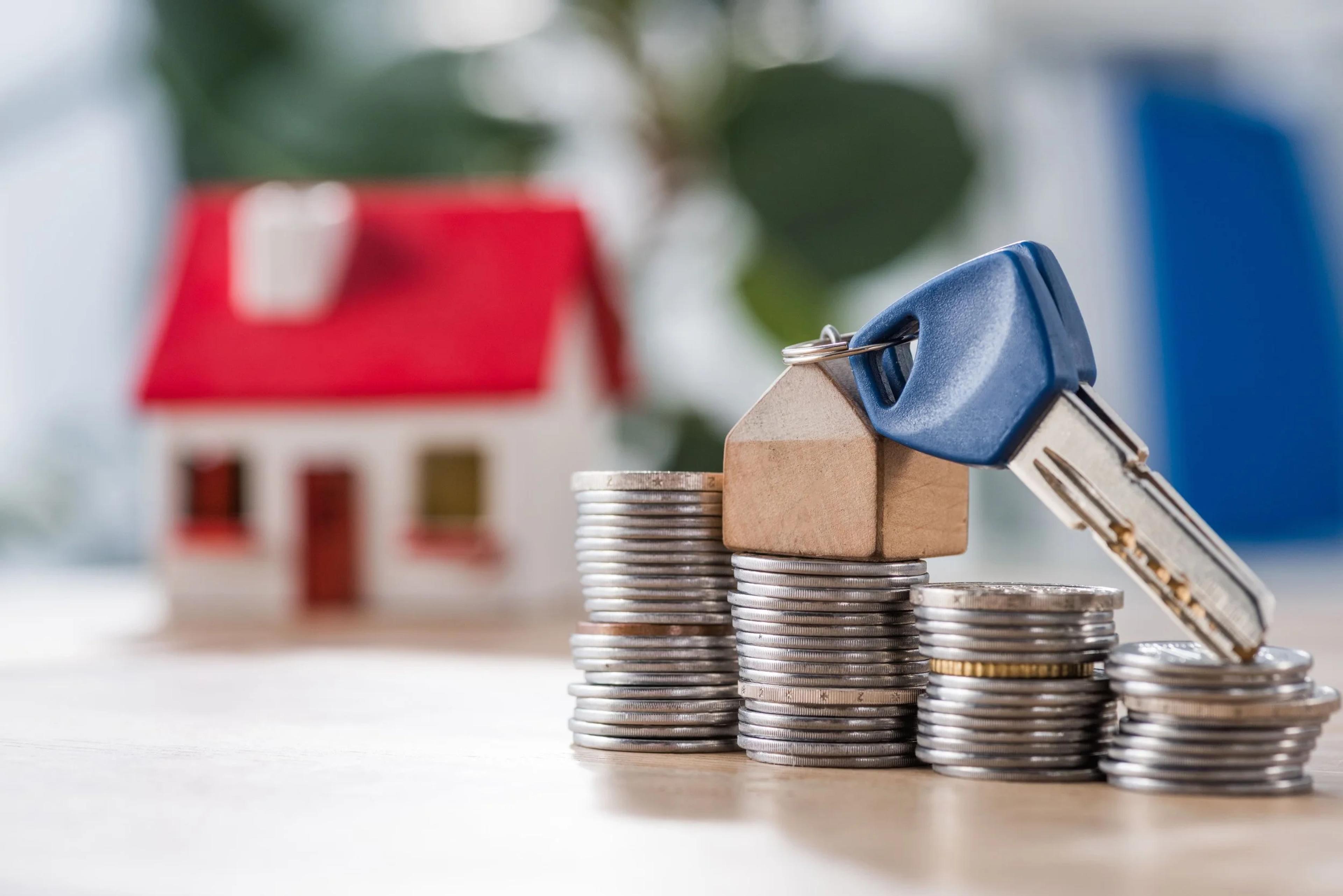 House keys on stacks of coins beside a model house