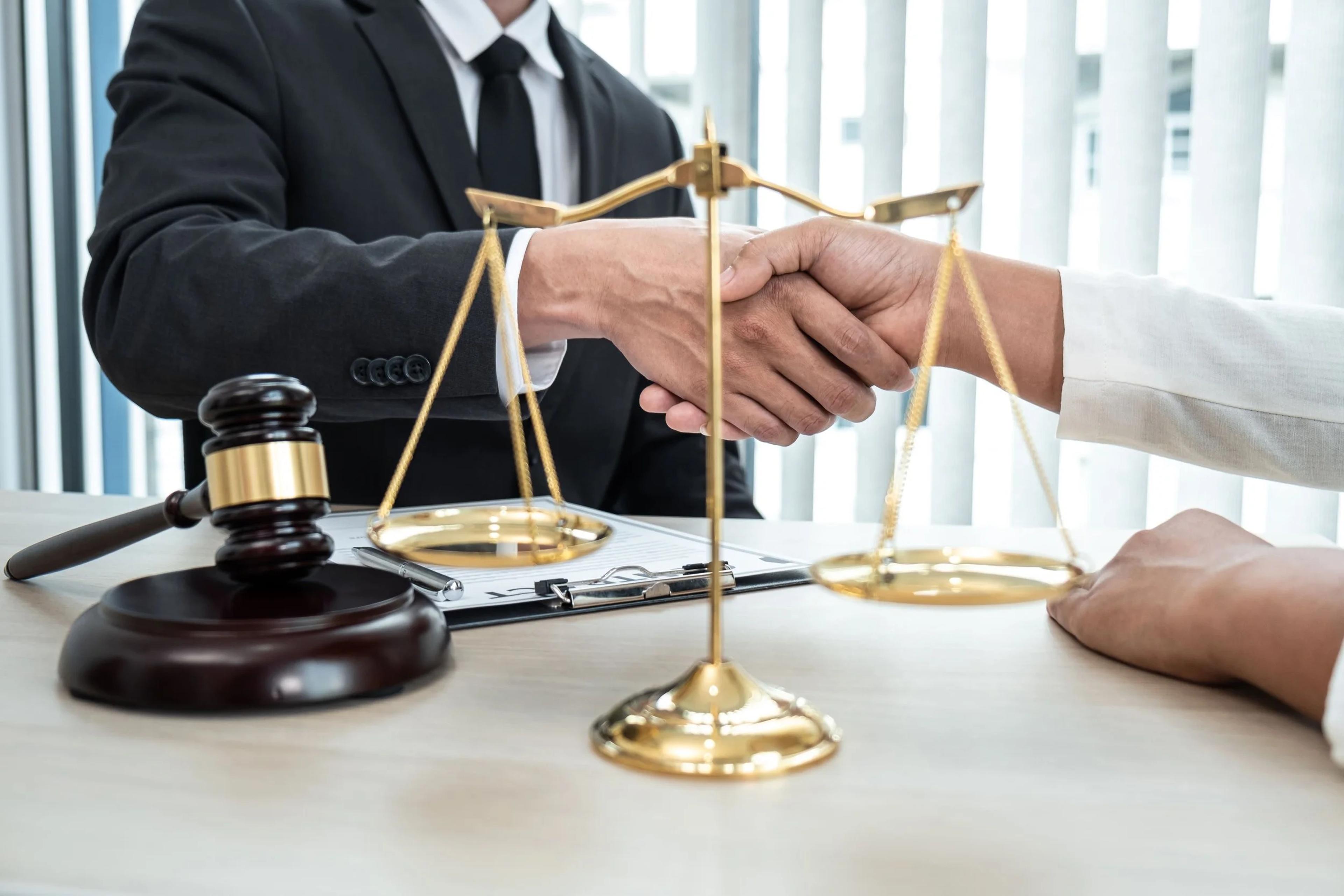 Handshake over a desk with legal scales and a gavel: legal checks in a property deal