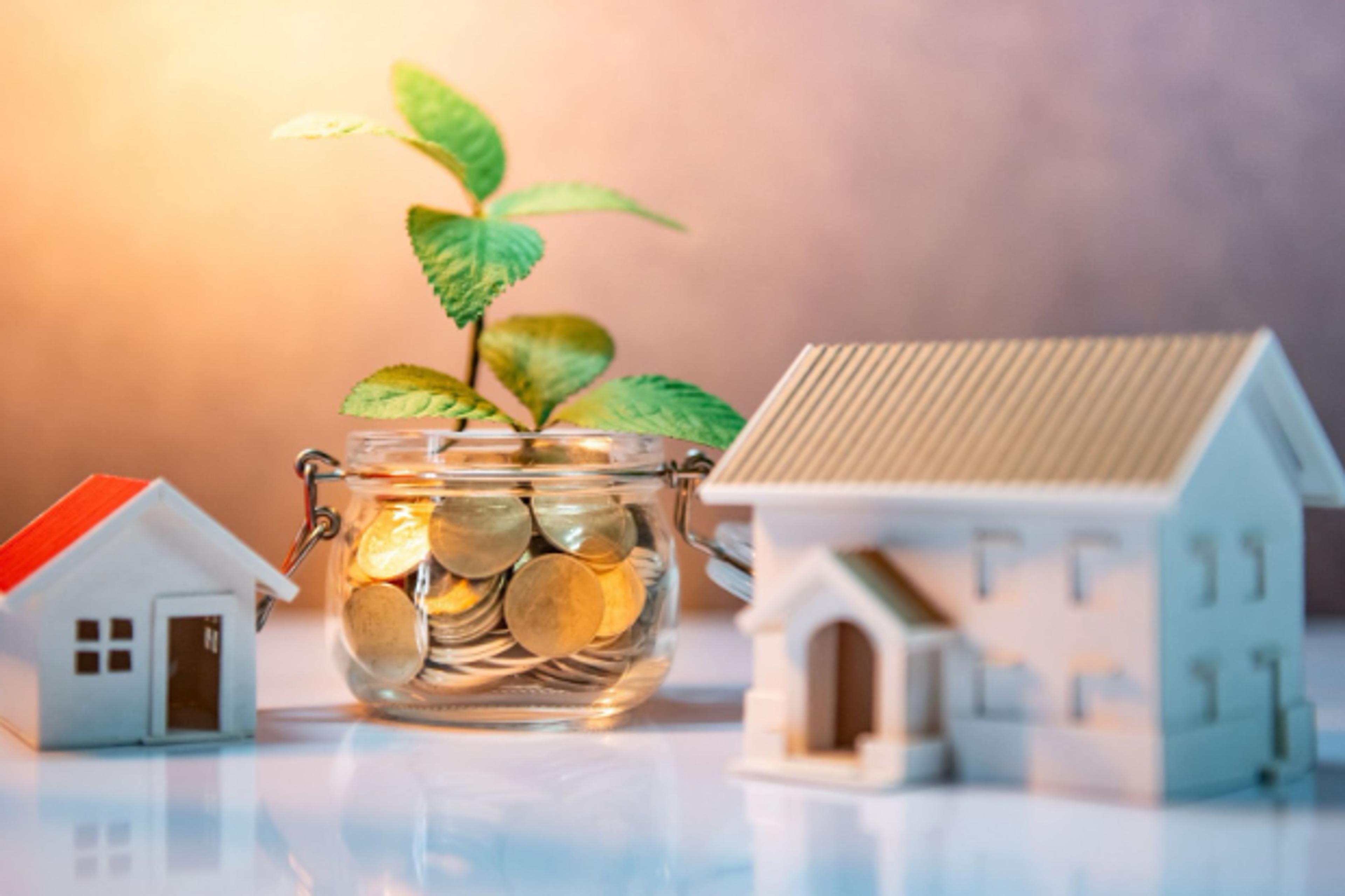 House models beside a jar of coins with a growing seedling: starting a property portfolio