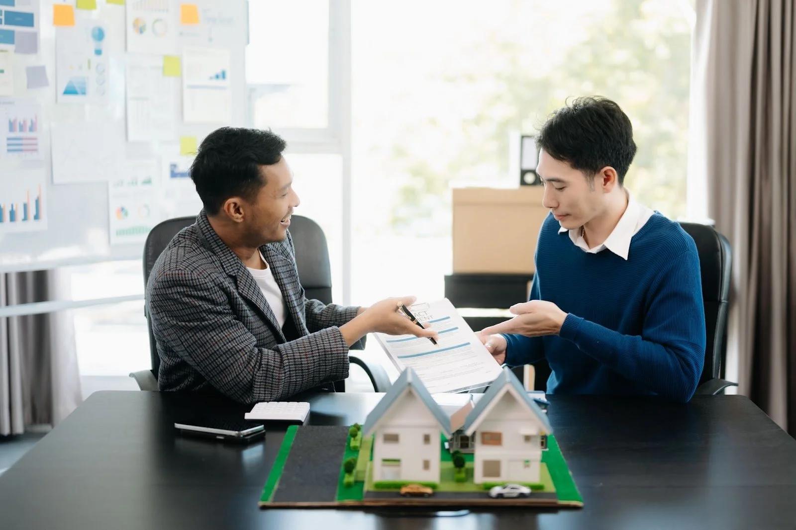 Property agent and seller reviewing sale documents beside house models
