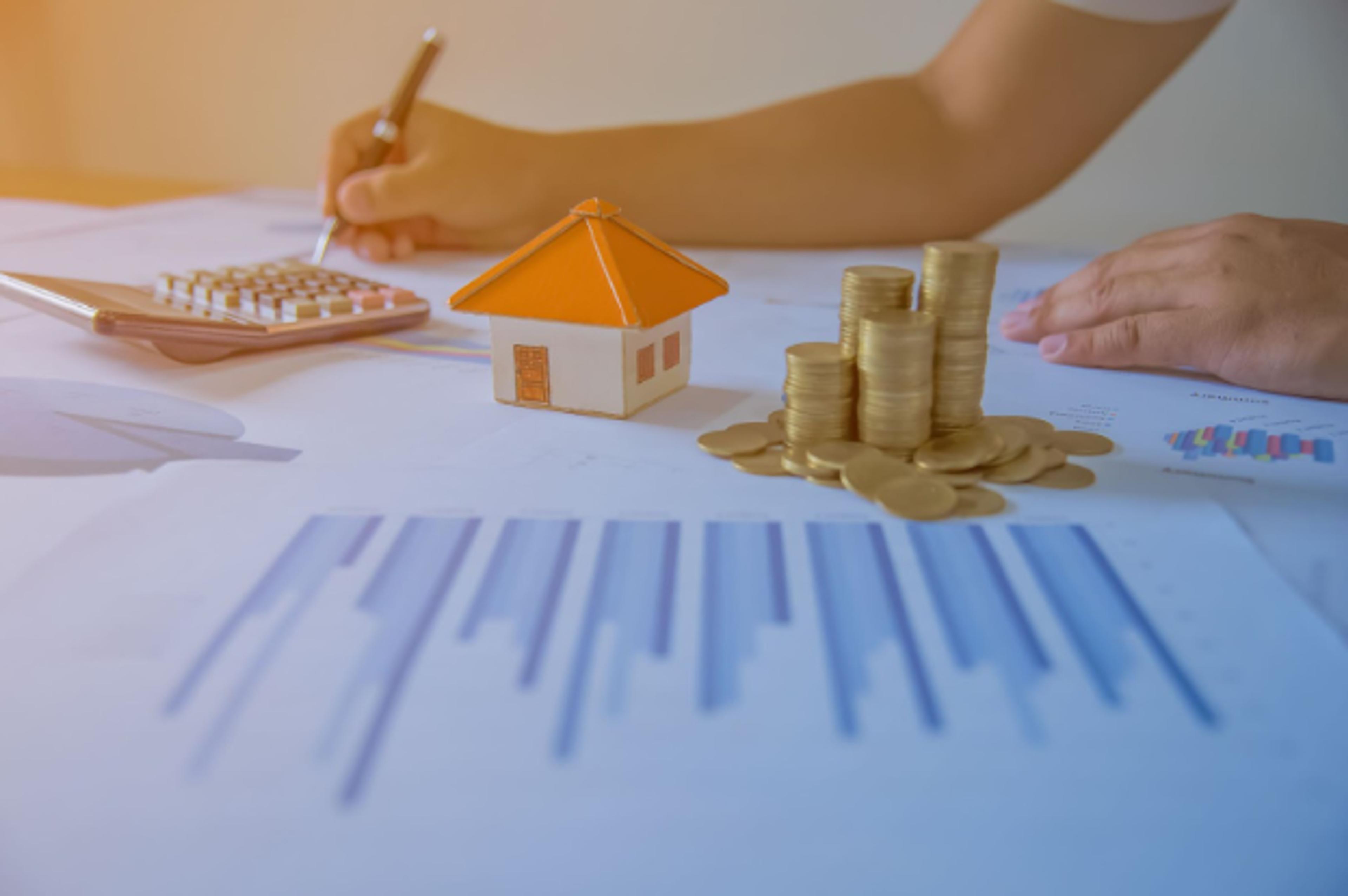 Signing property paperwork beside a house model, coins and a calculator