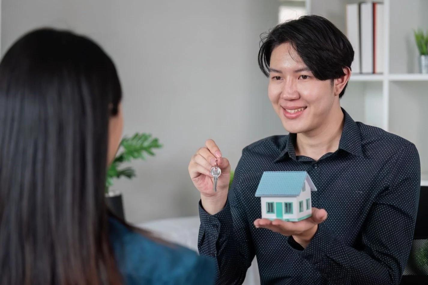 Seller handing house keys and a model home to the buyer