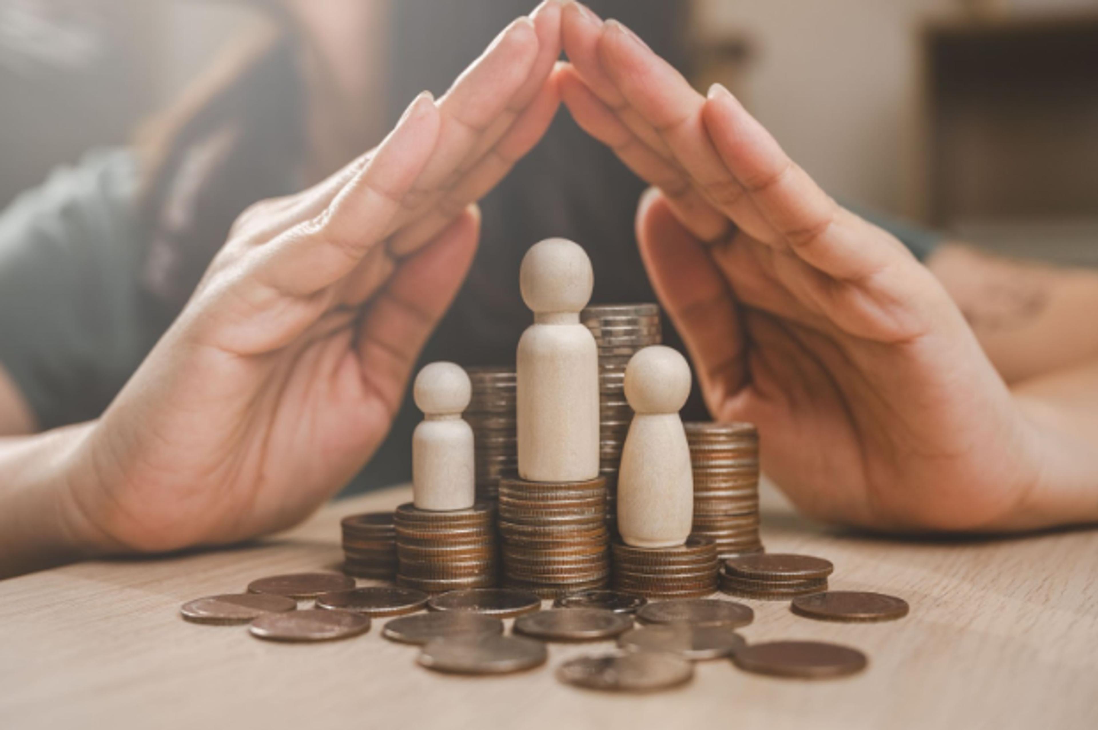 Hands forming a roof over wooden family figures standing on coins: protecting family wealth