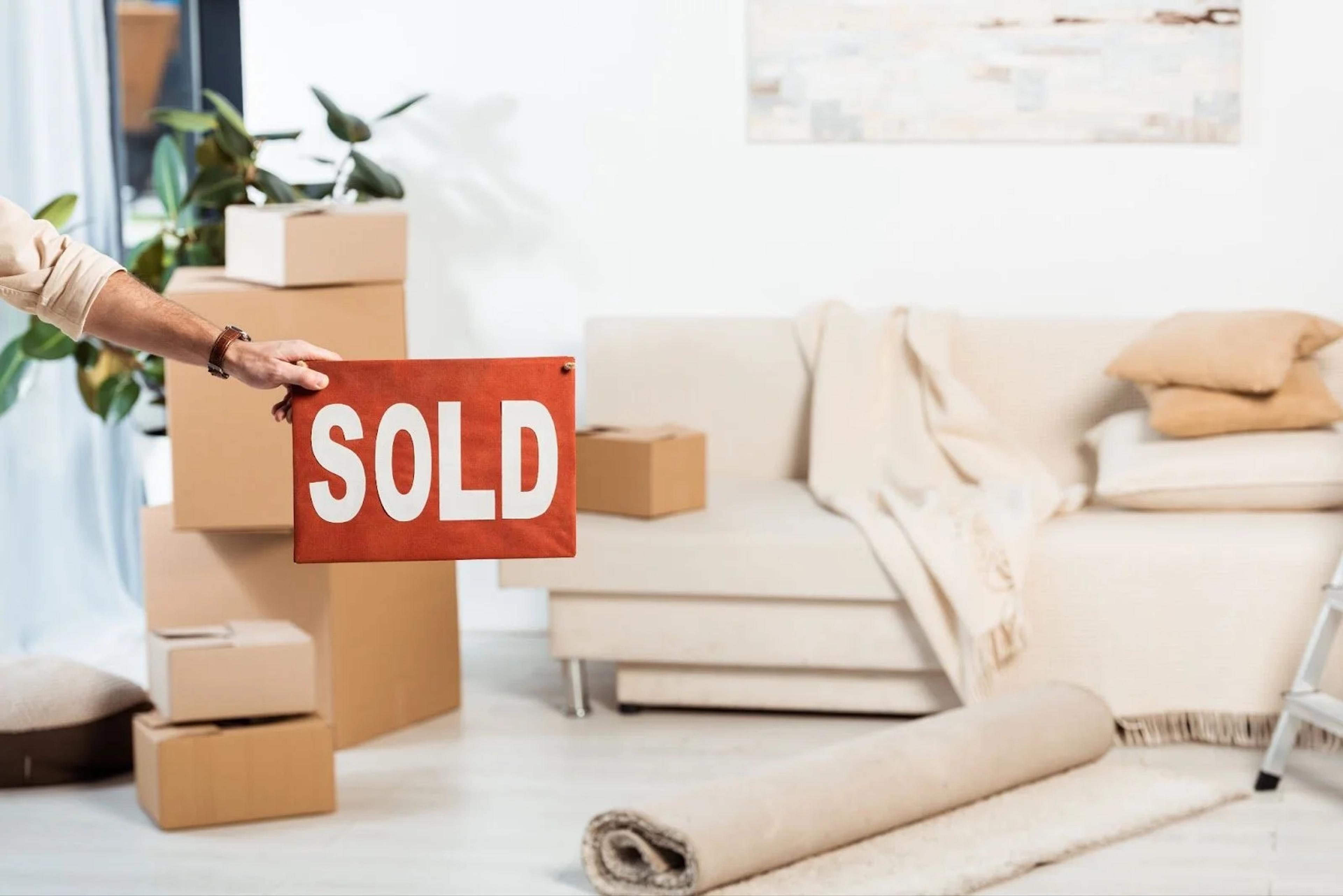 SOLD sign held up in a living room with packed moving boxes