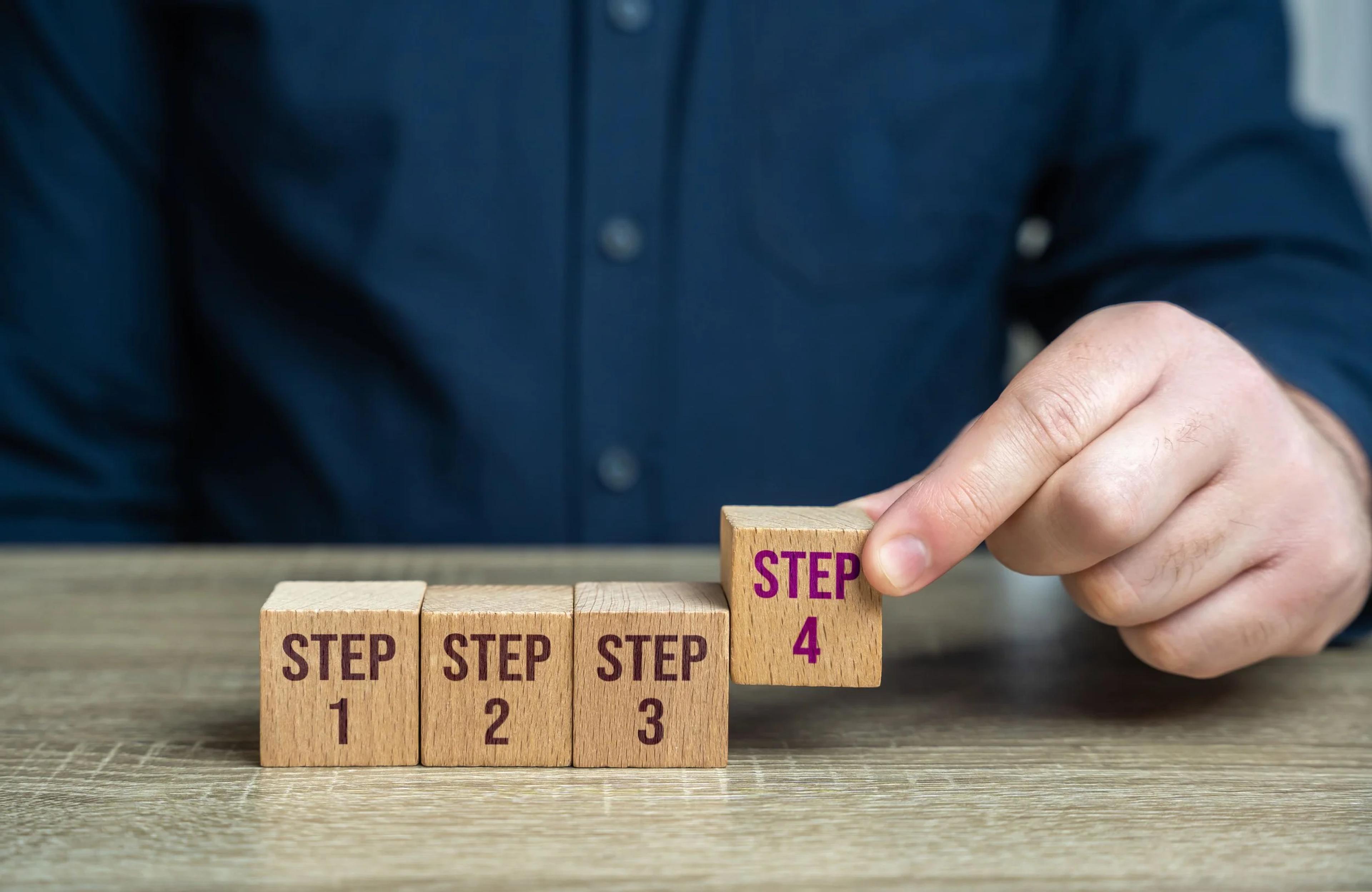 Hand placing wooden blocks for steps 1 to 4 of a property selling plan