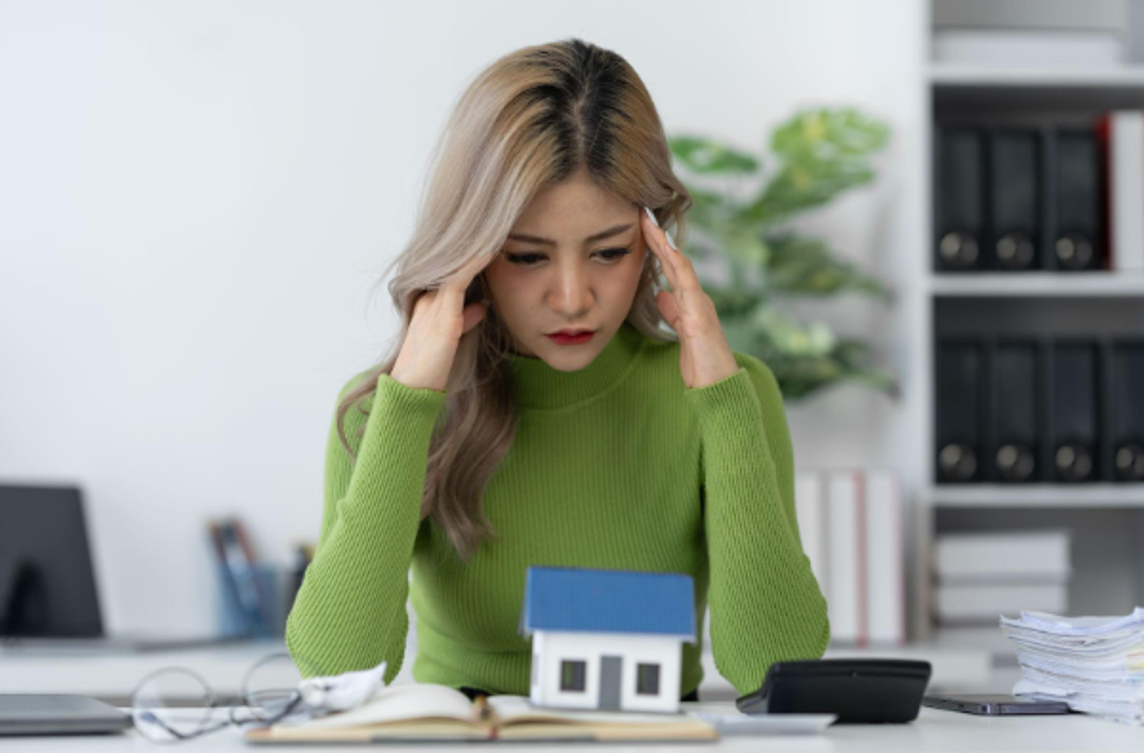 Worried woman with a house model and calculator, weighing up a condo purchase